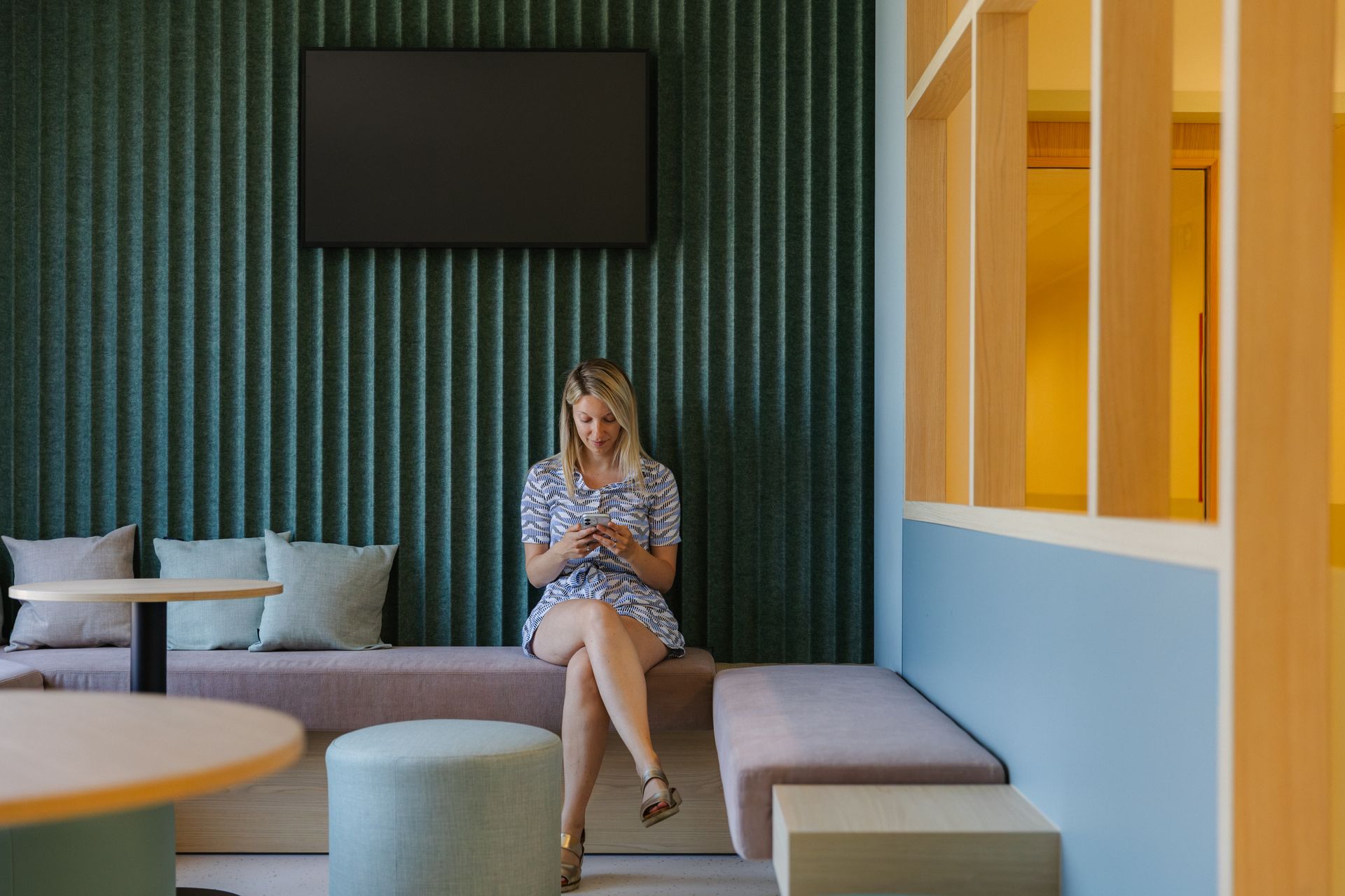 Vrouw zit op een gestoffeerde bank in een moderne woonkamer met groen gestreepte muren en een aan de muur gemonteerde tv.