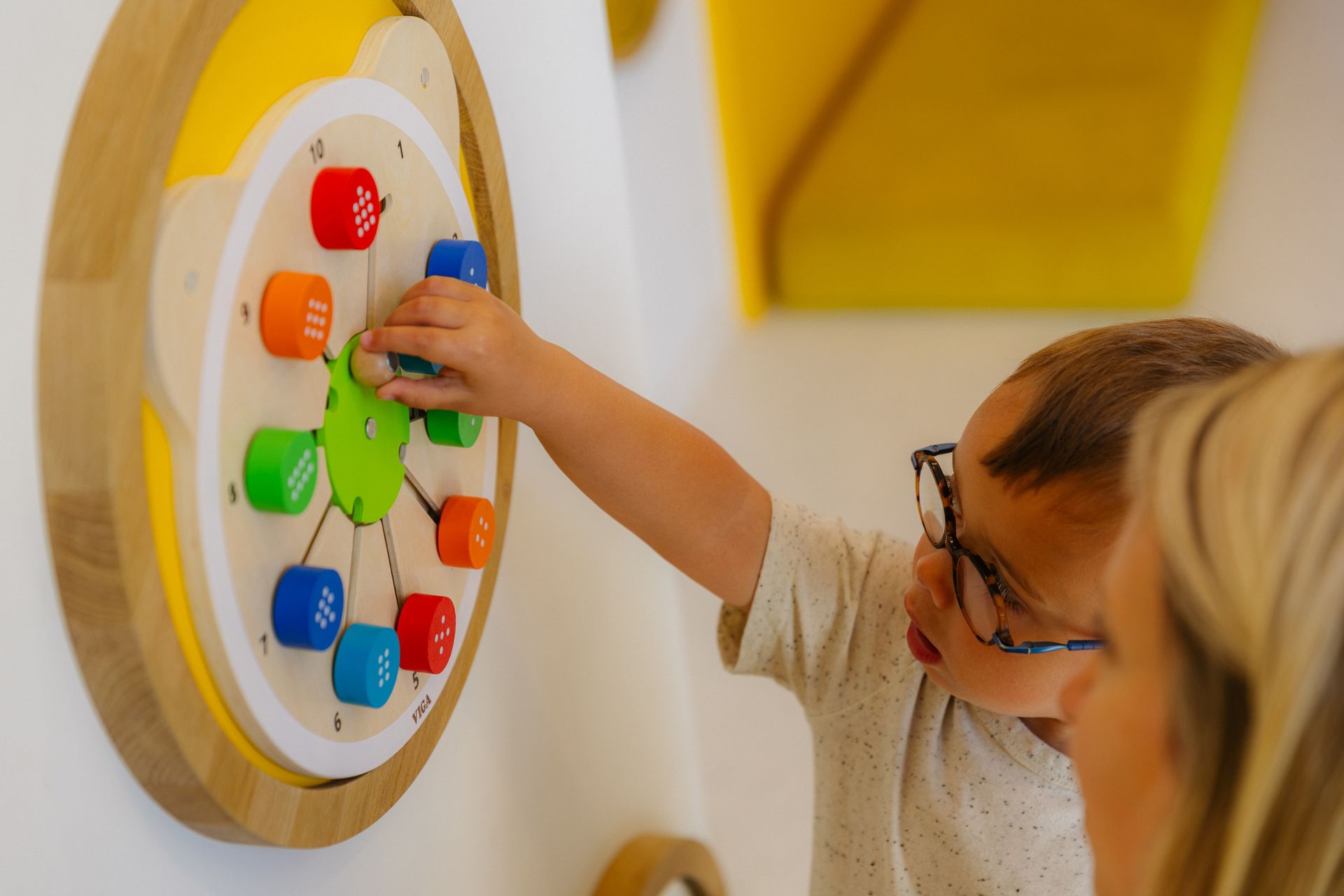 Kind speelt met een kleurrijk activiteitenbord aan de muur in een lichte kamer