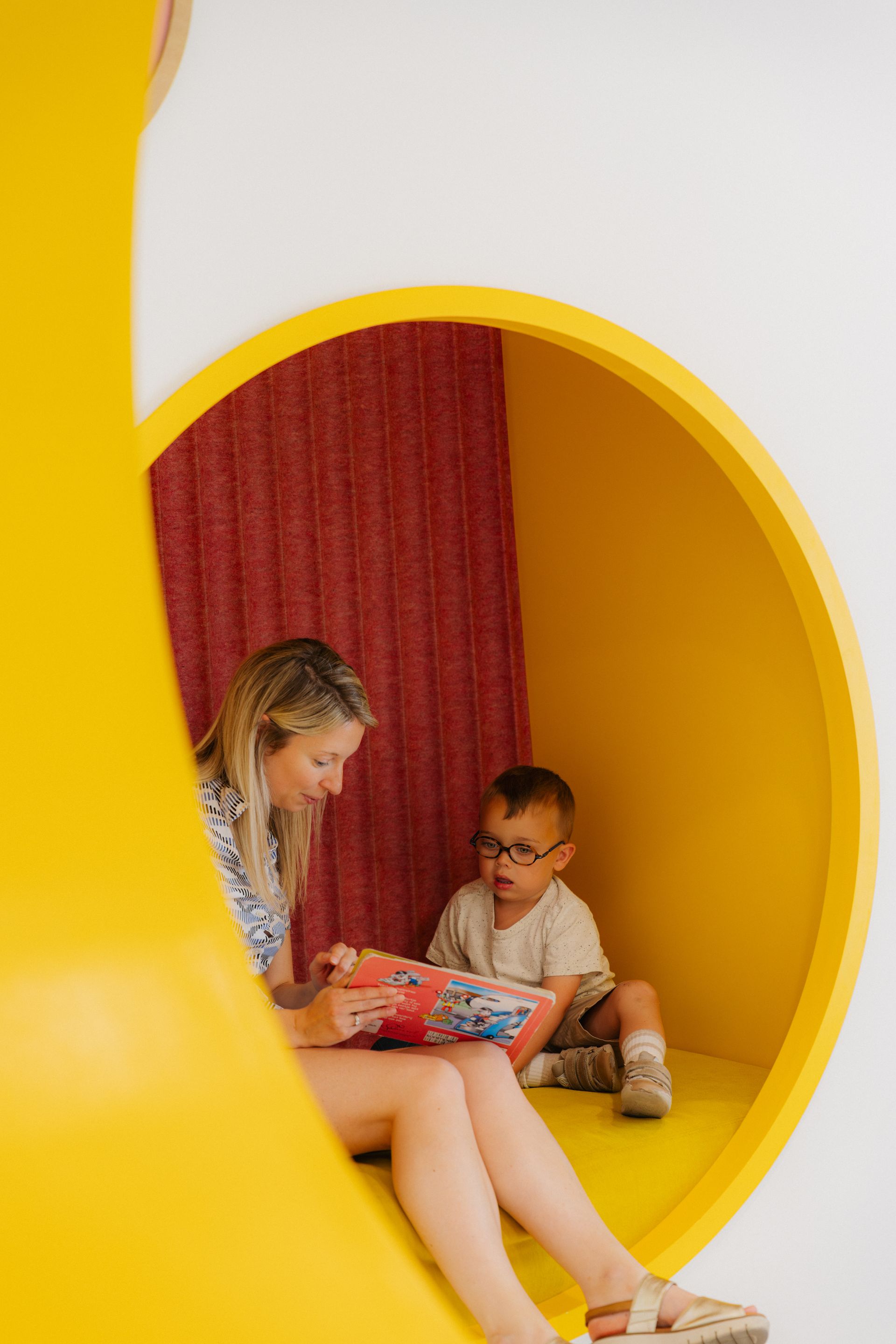 Twee kinderen zitten in een ronde, gele nis en kijken naar een tablet op de vloer.