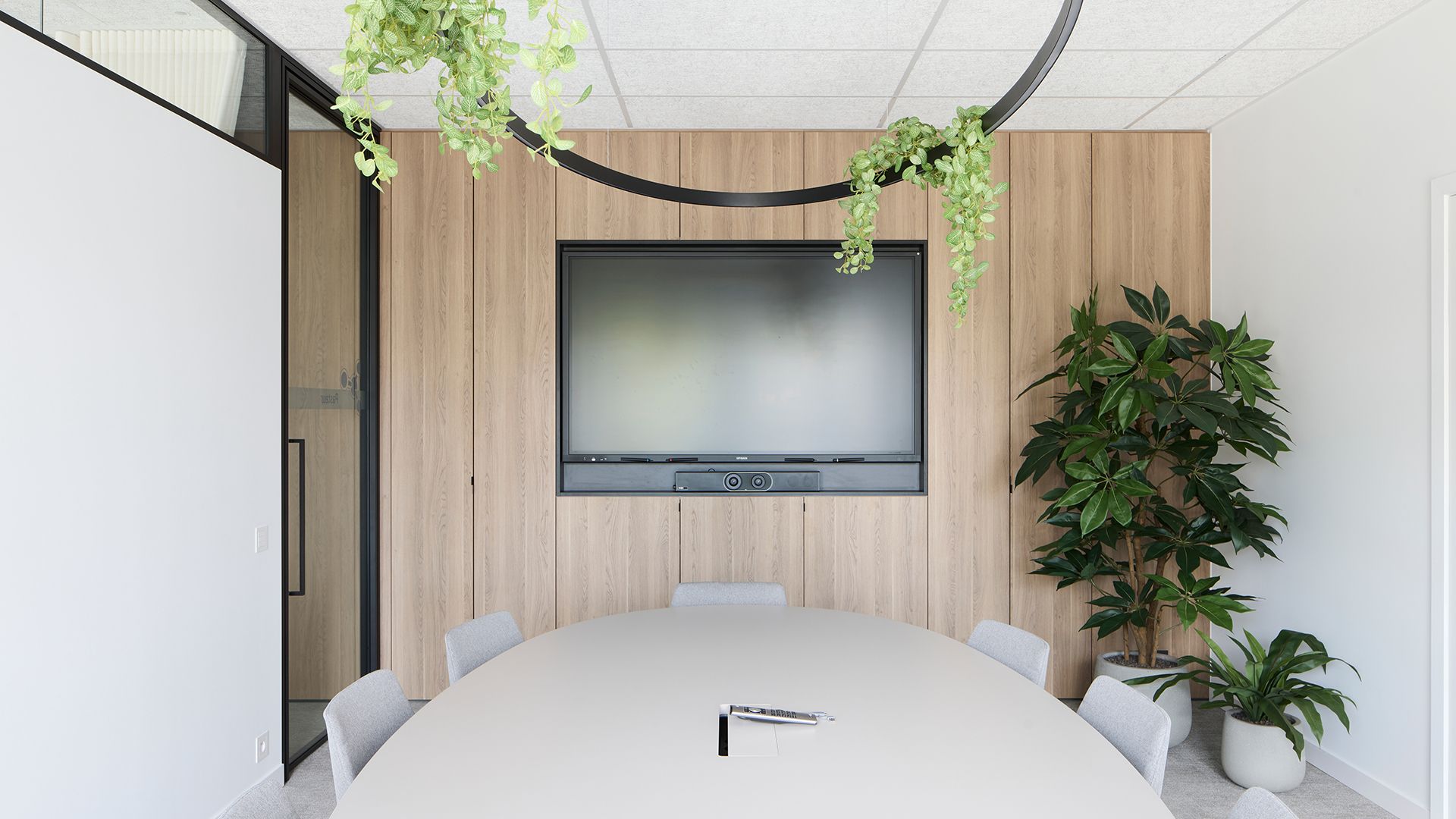 Moderne vergaderruimte met ronde tafel, tv aan de muur, houten accentmuur en hangplanten