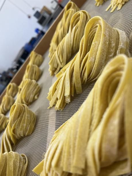 Bündel frischer, gelber Tagliatelle-Nudeln trocknen auf einer Oberfläche, möglicherweise in einer Großküche.