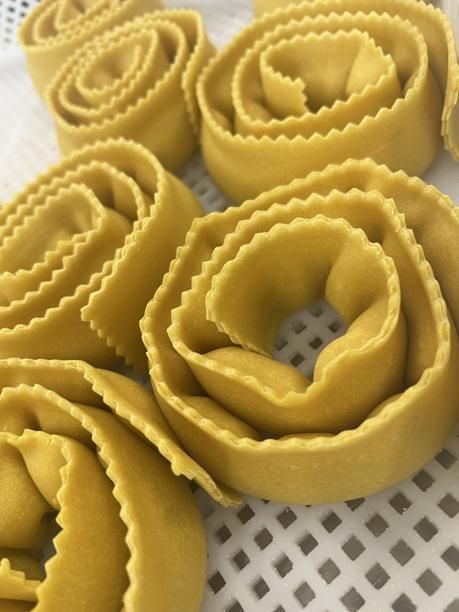 Gelbe, zu rosenartigen Spiralen geformte Nudeln, die auf einer weißen, geschlitzten Oberfläche liegen.