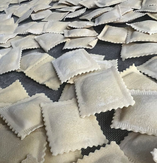 Gnocchi mit Tomatensoße, Basilikum und Parmesan auf einem weißen Teller, mit Brot, Tomaten, Gabel und Messer auf einem Holztisch.