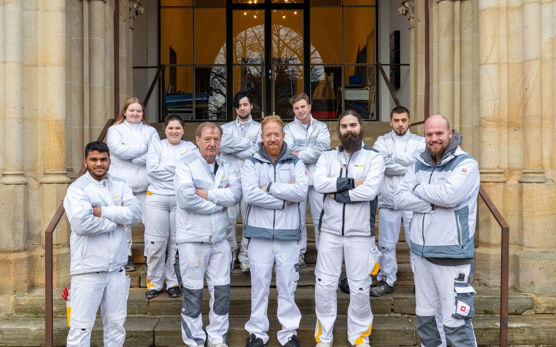 Eine Gruppe von Menschen in weißen Overalls posiert vor einem Gebäude für ein Foto.
