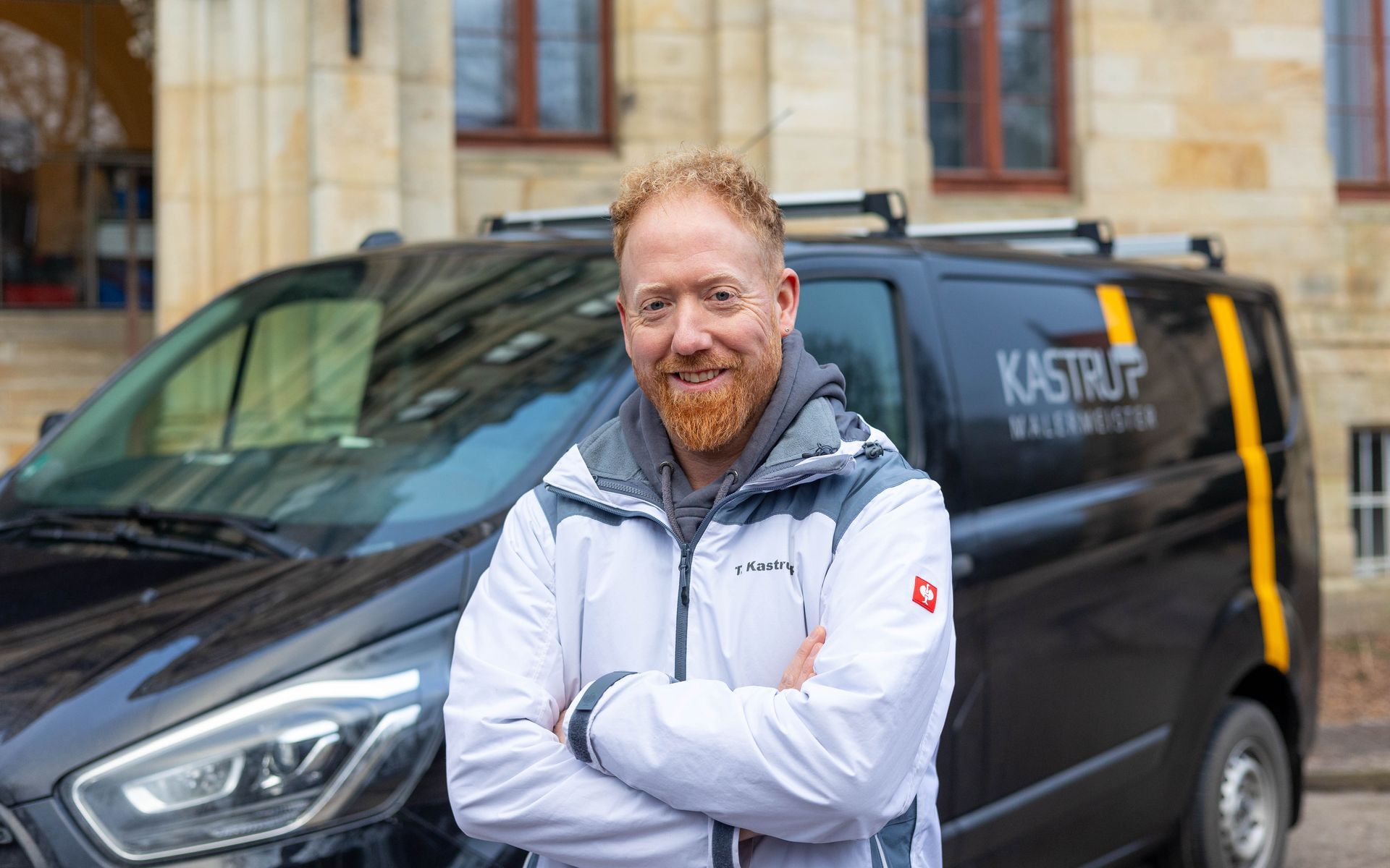 Ein Mann mit Bart steht mit verschränkten Armen vor einem Lieferwagen.