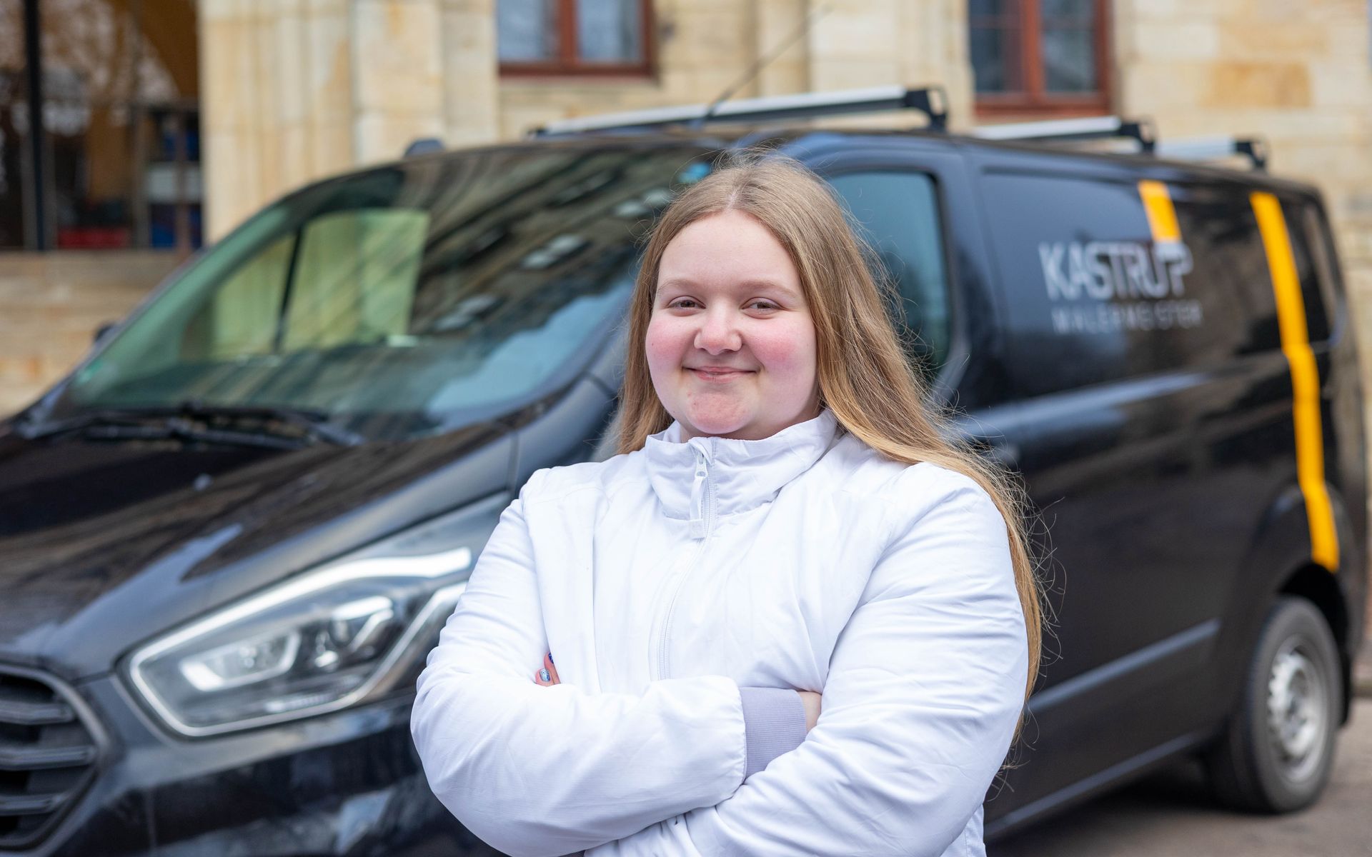 Eine Frau steht mit verschränkten Armen vor einem schwarzen Lieferwagen.