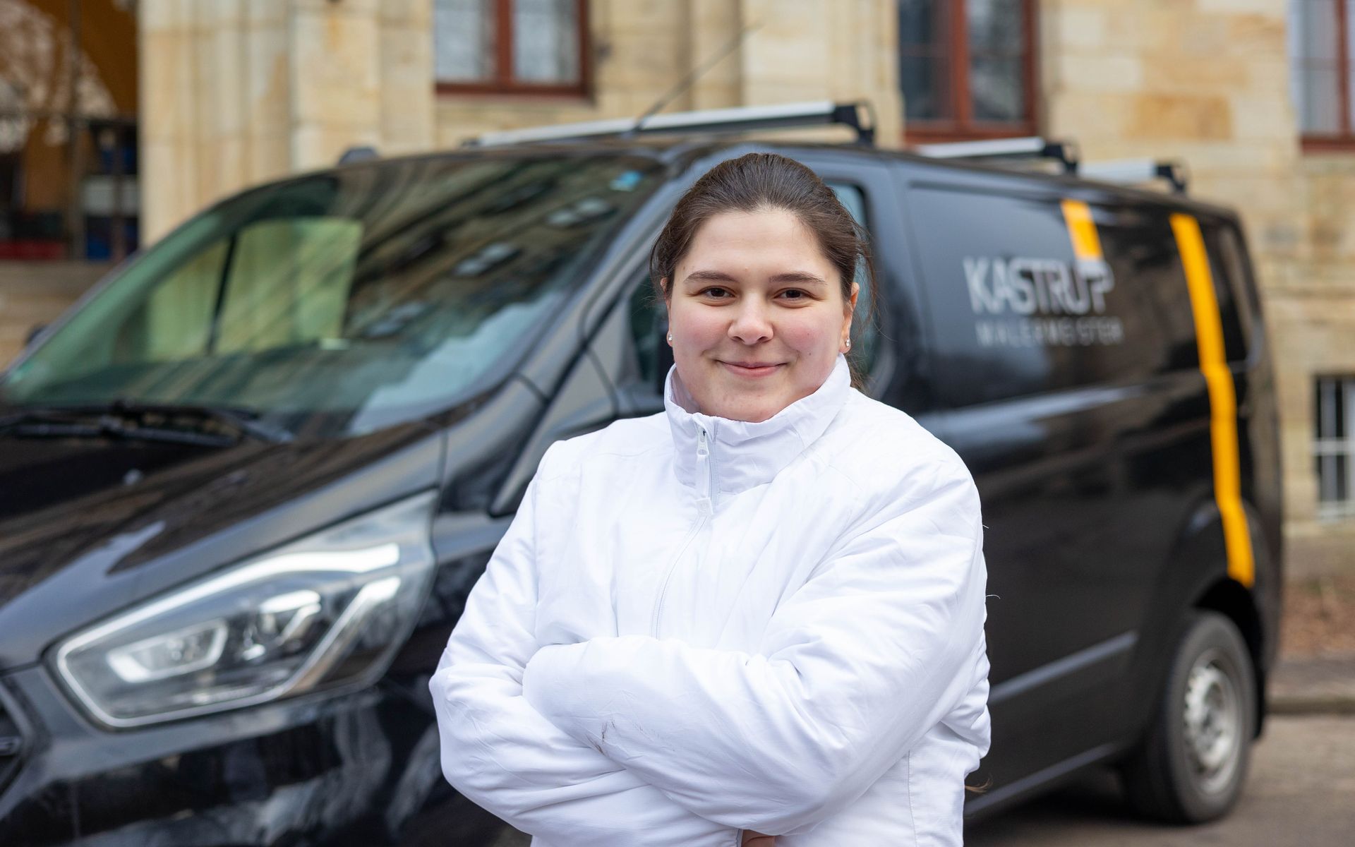 Eine Frau steht mit verschränkten Armen vor einem schwarzen Lieferwagen.