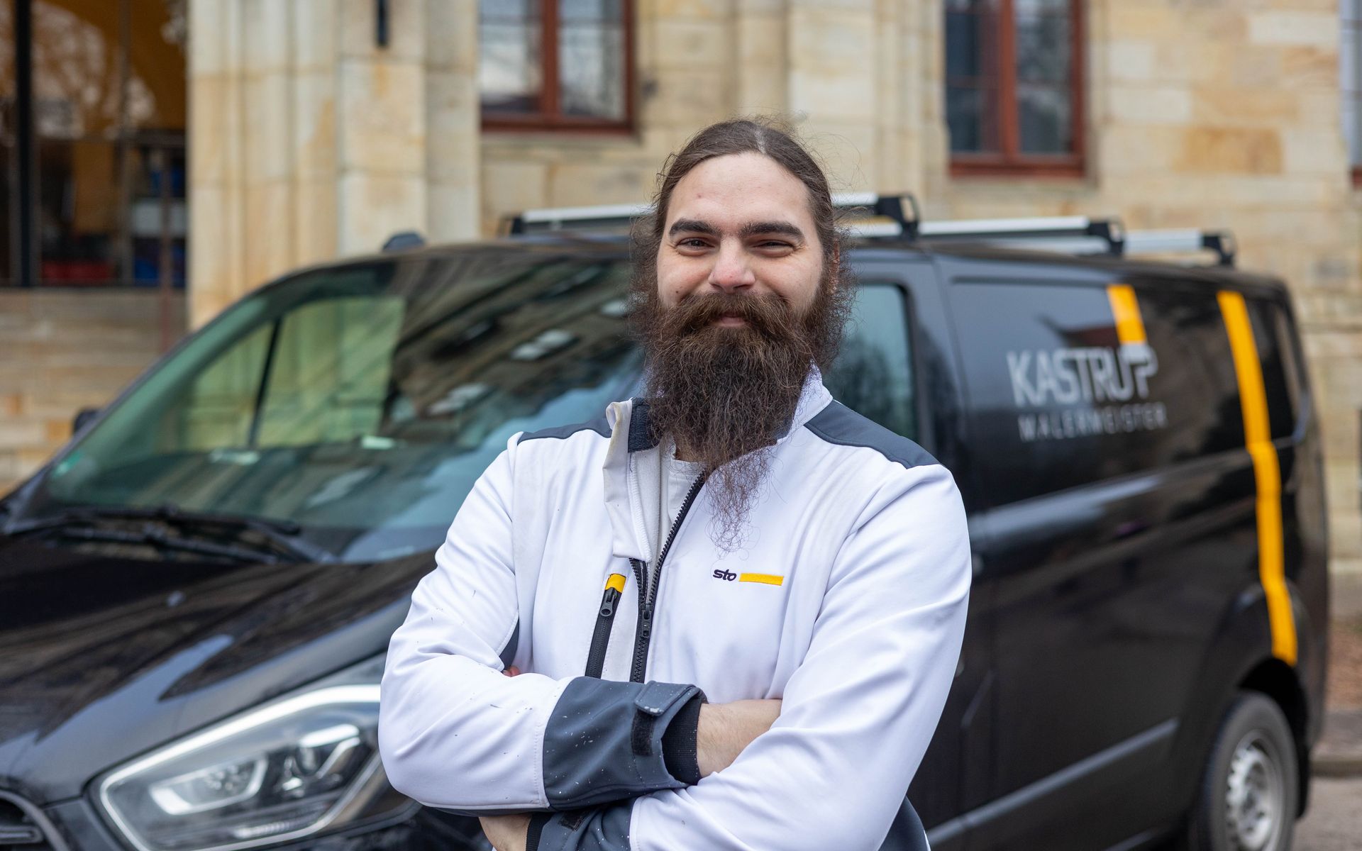 Ein Mann mit Bart steht vor einem Lieferwagen.