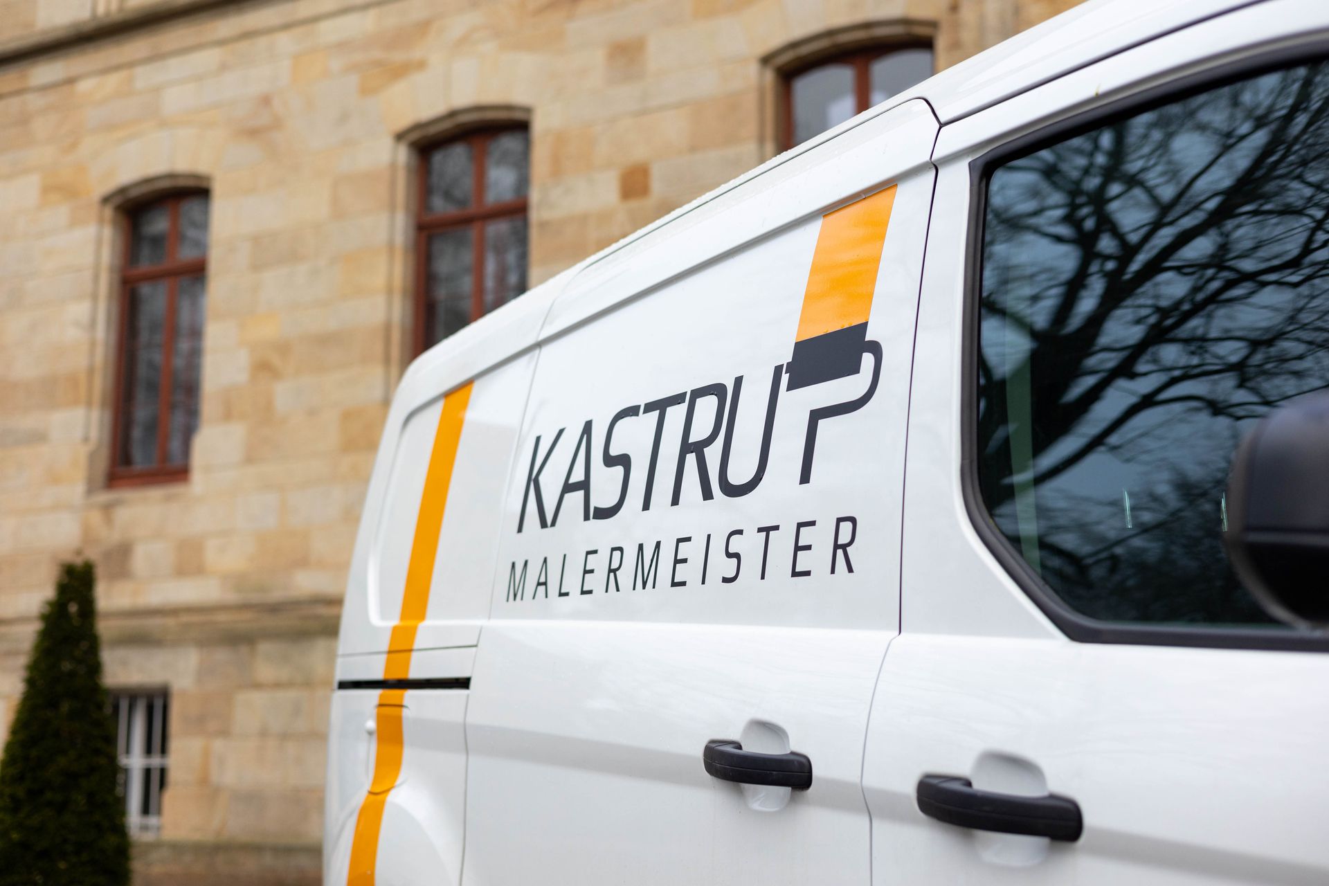 Ein weißer Lieferwagen mit der Aufschrift „Kastrup Malermeister“ an der Seite steht vor einem Gebäude.