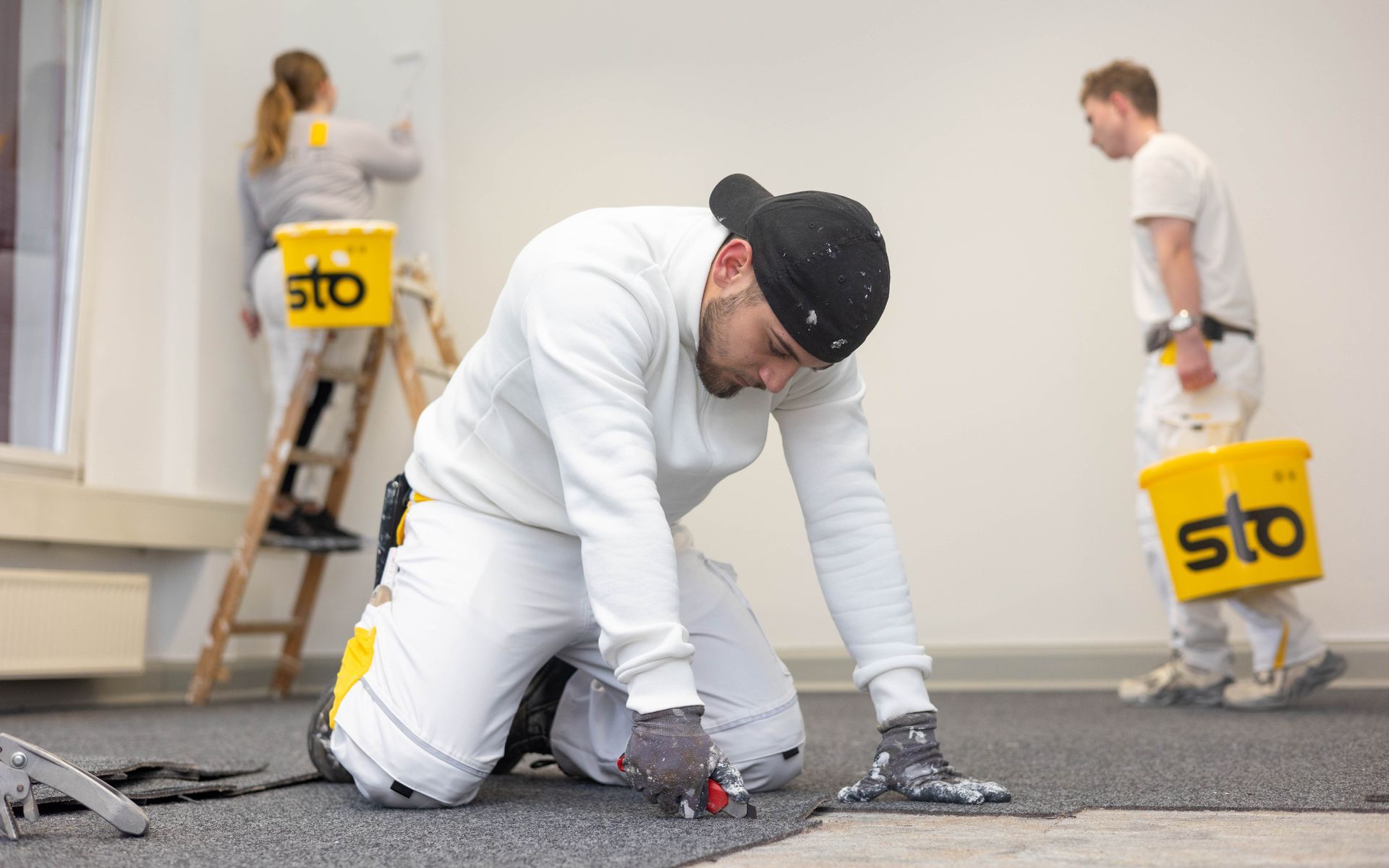 Ein Mann kniet nieder, während er in einem Zimmer eine Wand streicht.