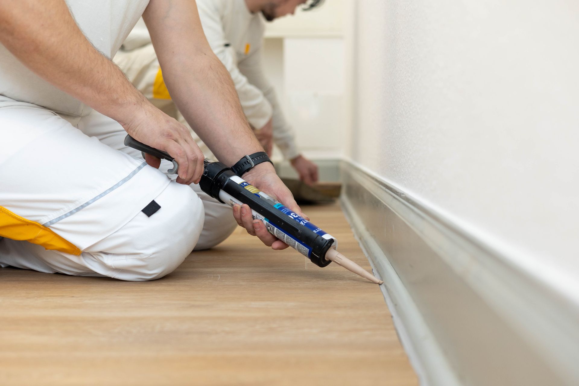 Ein Mann kniet nieder und trägt Dichtungsmasse auf eine Wand auf.