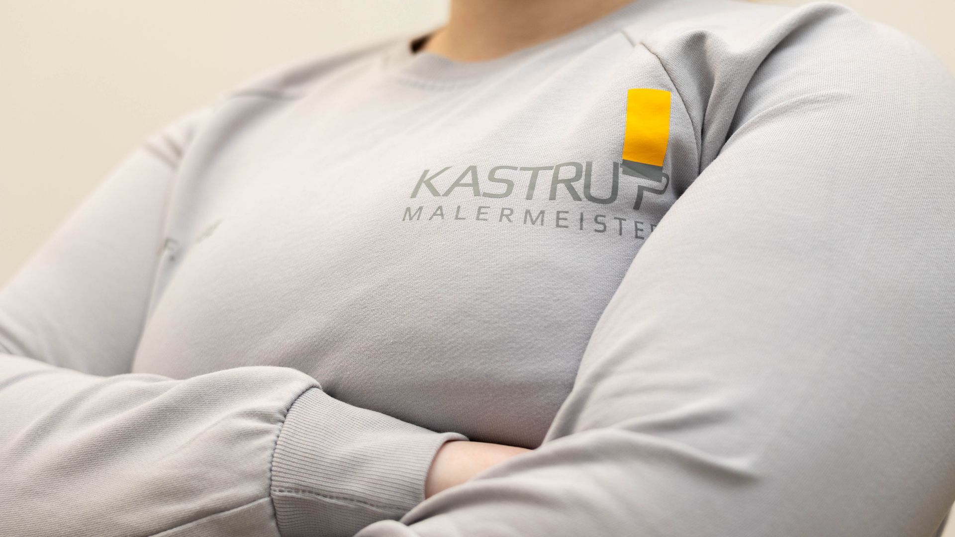 Eine Nahaufnahme einer Person, die ein graues Hemd mit der Aufschrift „Kastrup Malermeister“ trägt