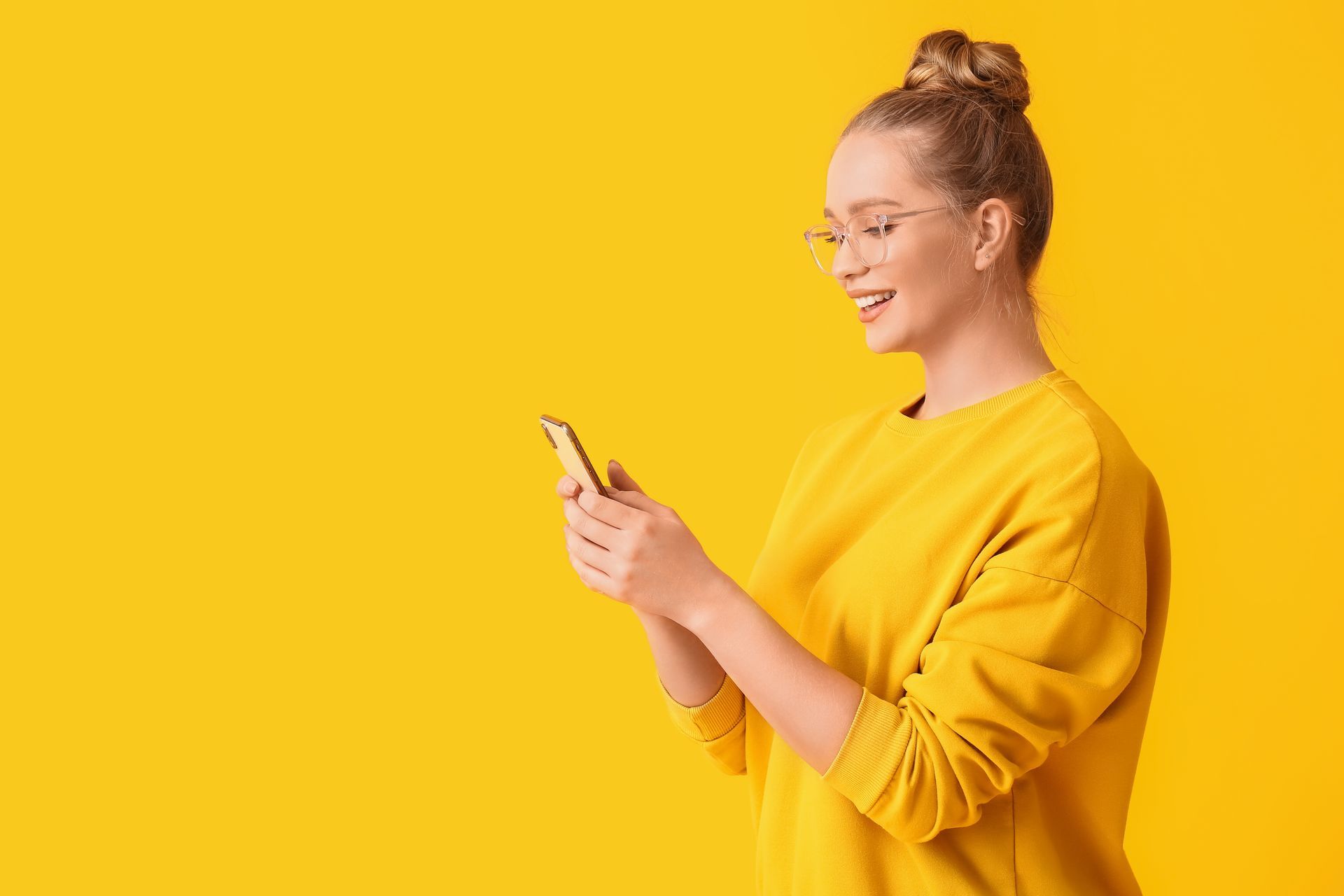 Eine Frau in einem gelben Pullover benutzt ein Mobiltelefon.