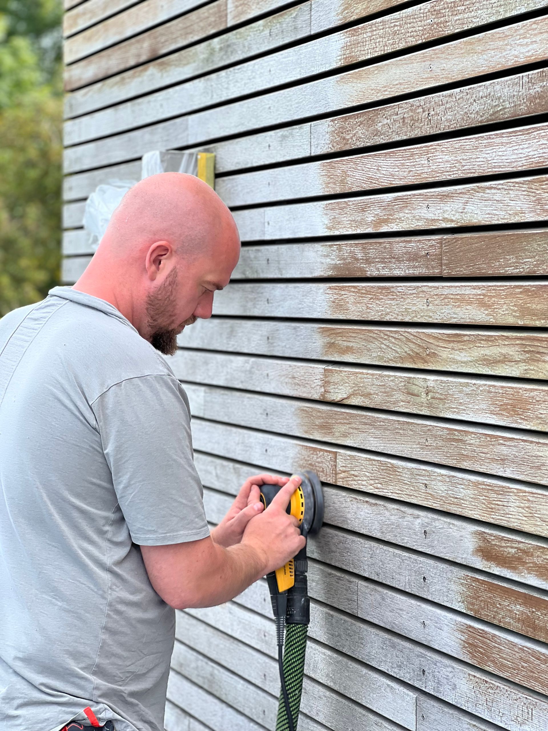 Ein Mann schleift mit einem Schleifgerät eine Holzwand.