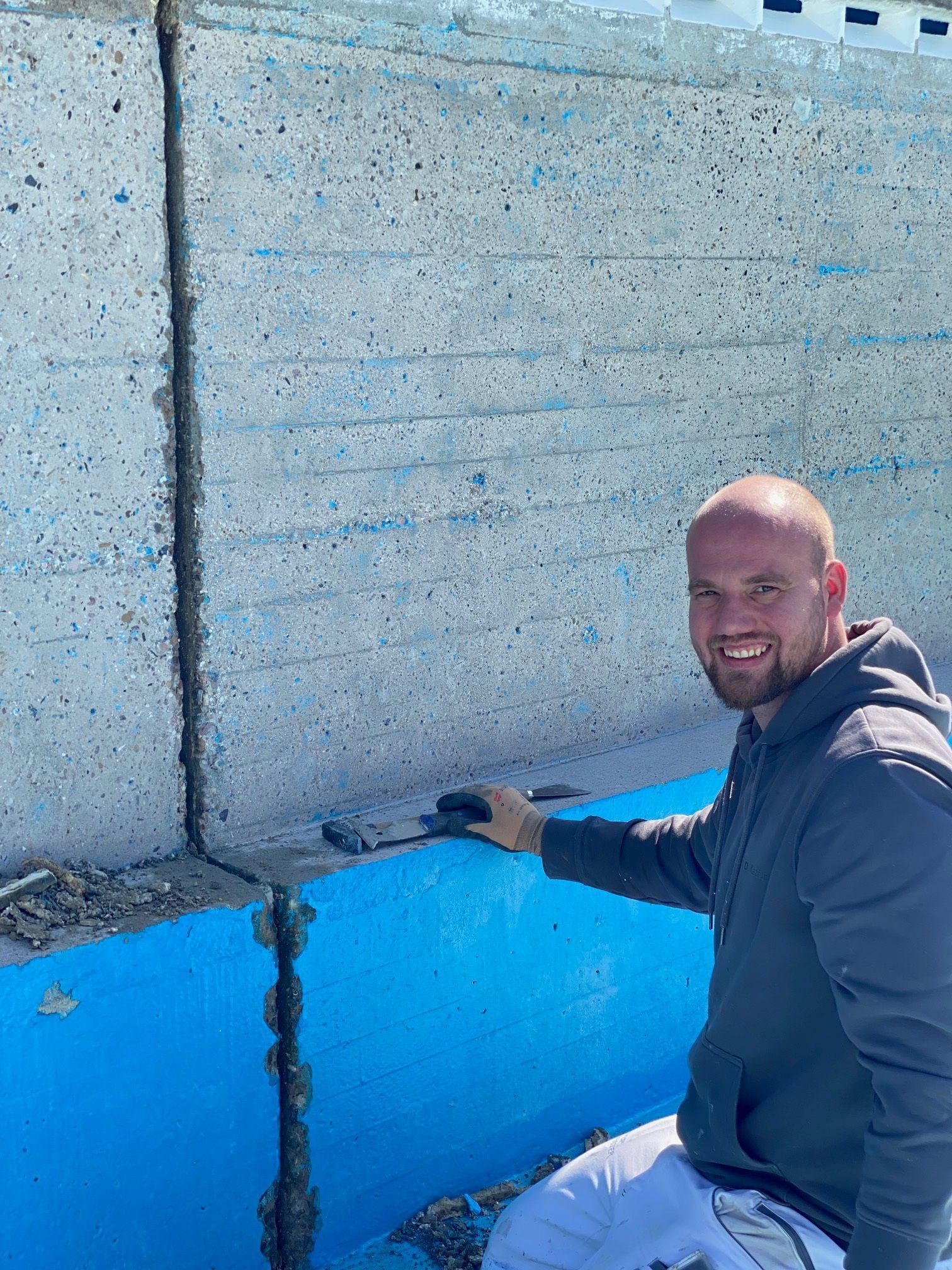 Ein Mann arbeitet an einer Betonmauer neben einem blauen Pool.