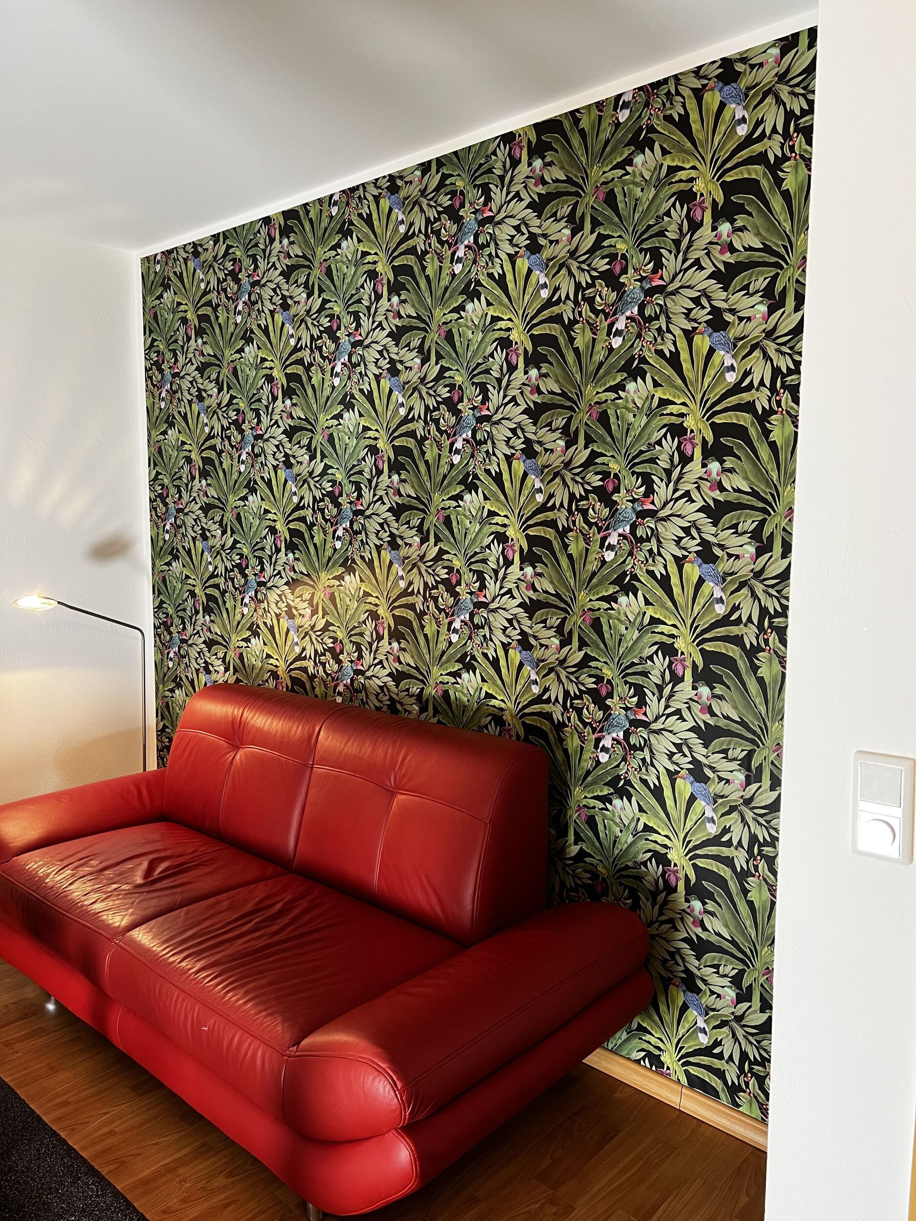 Ein rotes Sofa steht vor einer Wand mit gemusterter Tapete.