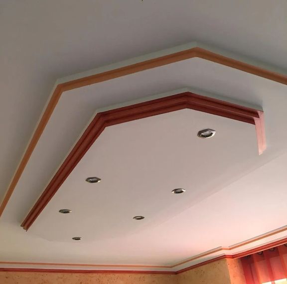 Plafond blanc avec moulures en bois superposées et éclairage encastré dans une pièce