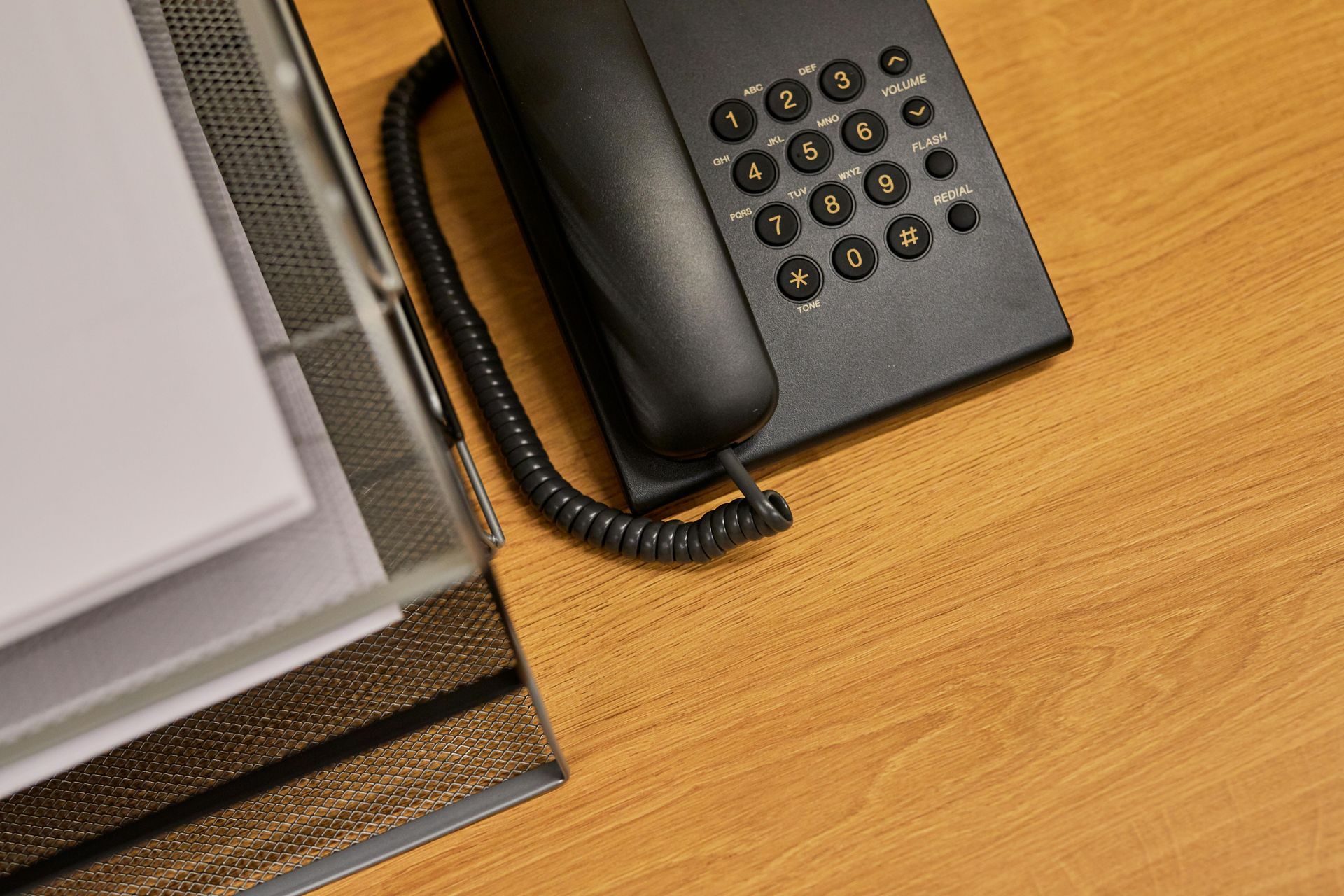 Un téléphone de bureau à côté d'une pile de papiers sur un bureau en bois