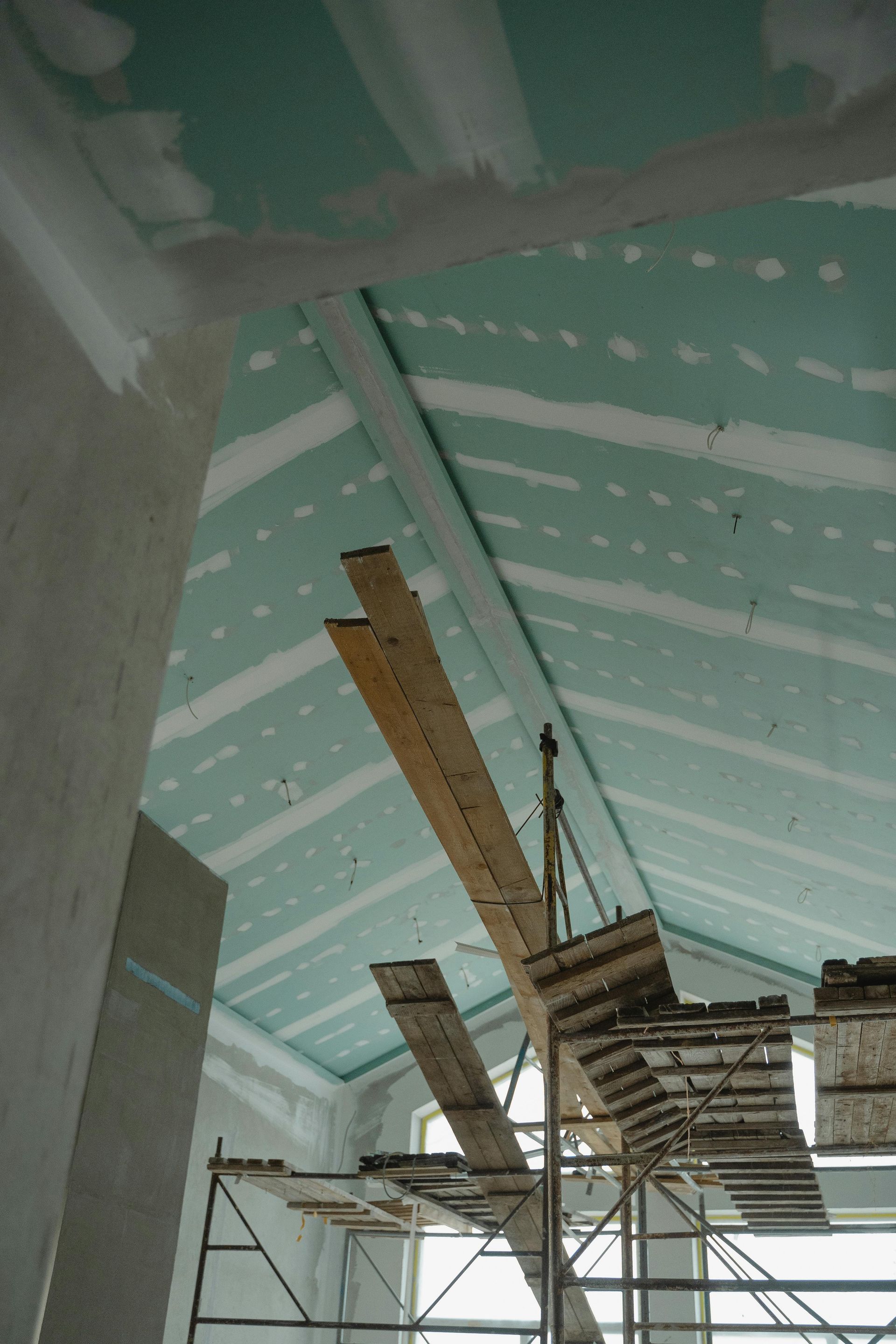 Plafond en construction avec panneaux isolants turquoise et poutres apparentes dans un intérieur inachevé
