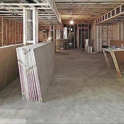 Sous-sol non aménagé avec charpente apparente, piles de plaques de plâtre et matériaux de construction au sol