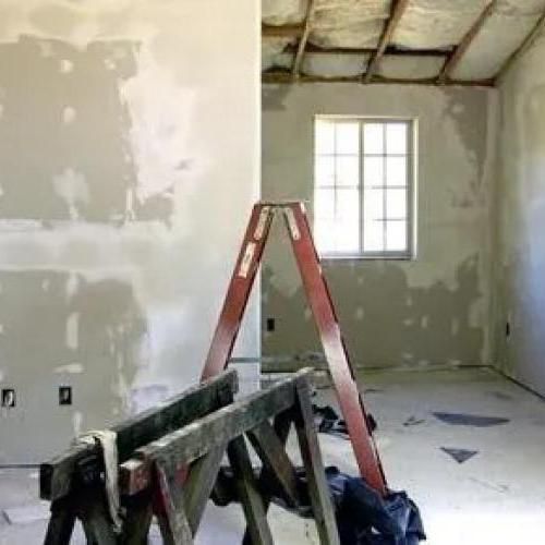 Pièce en rénovation avec une échelle rouge, des plaques de plâtre réparées et des poutres apparentes au plafond.