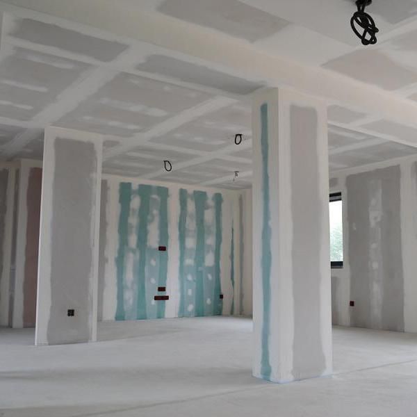 Pièce intérieure inachevée avec cloisons sèches blanches, joints de couleur turquoise et luminaires apparents au plafond.