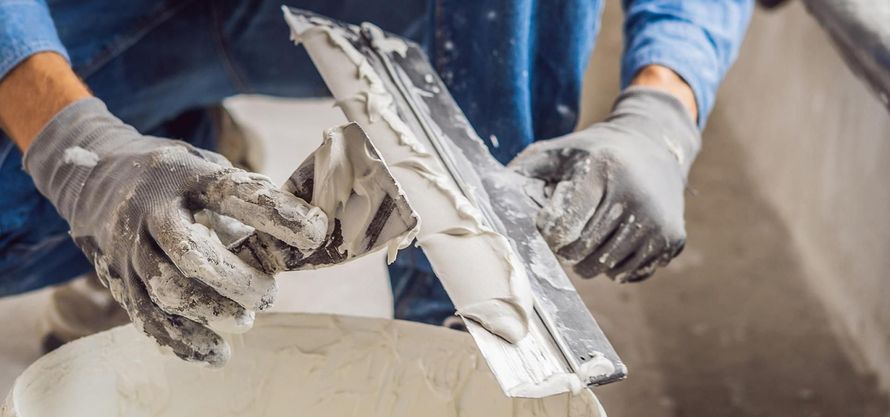 Des mains gantées appliquent du plâtre sur un mur à l'aide d'une truelle sur un chantier de construction