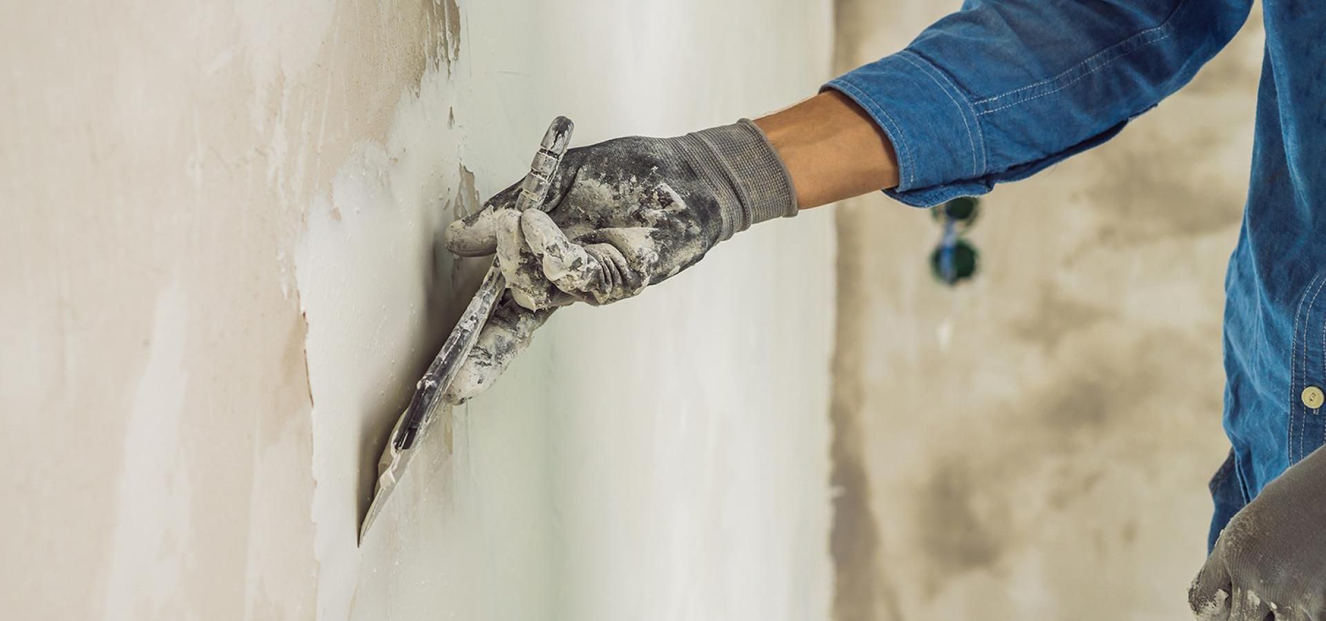 Main gantée appliquant du plâtre à la truelle sur un mur lors de travaux de réparation intérieure