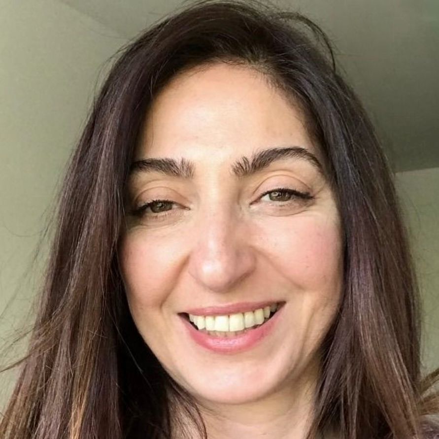 Eine Frau mit braunem Haar und blauen Augen lächelt in die Kamera.