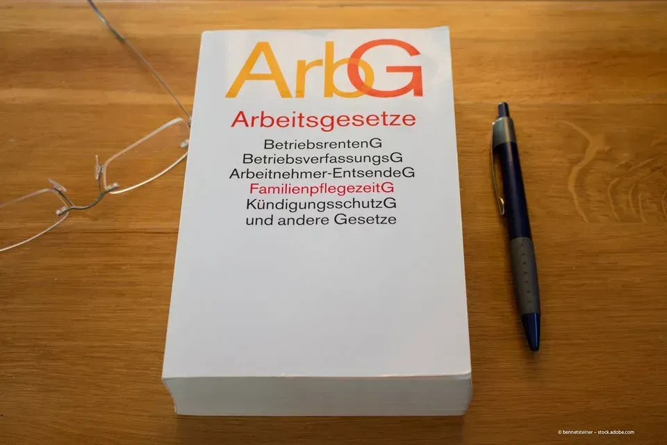 In einer Anwaltskanzlei liegt das Arbeitsgesetzbuch auf einem Schreibtisch, daneben eine Brille und ein Kugelschreiber.