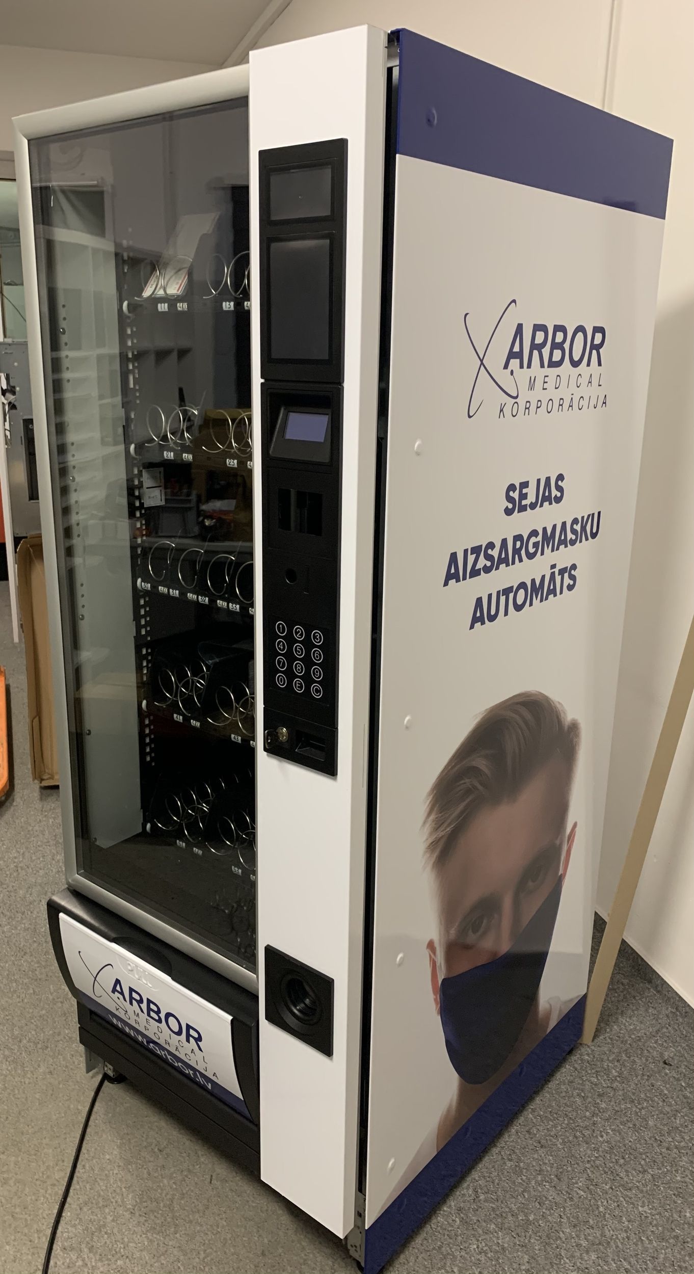 Weißer ARGO-Verkaufsautomat mit Glasfront, blauer Umrandung und seitlicher Werbung in einem Ausstellungsraum oder Büroflur