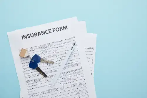 A stack of insurance forms with keys and a pen on a blue background.
