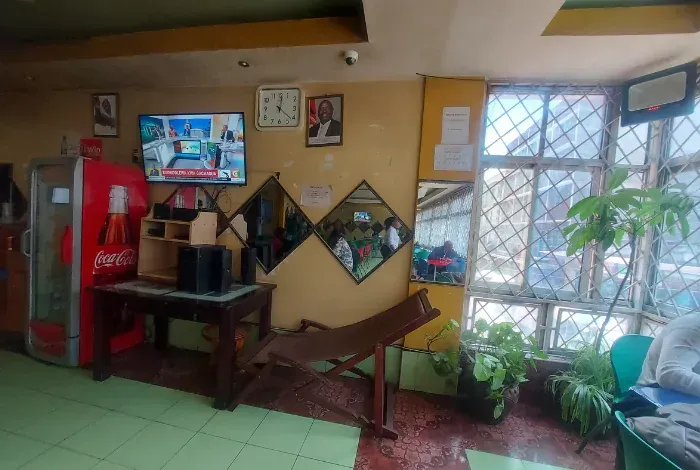 A room with a coca cola cooler , a tv , a bench , and a mirror.