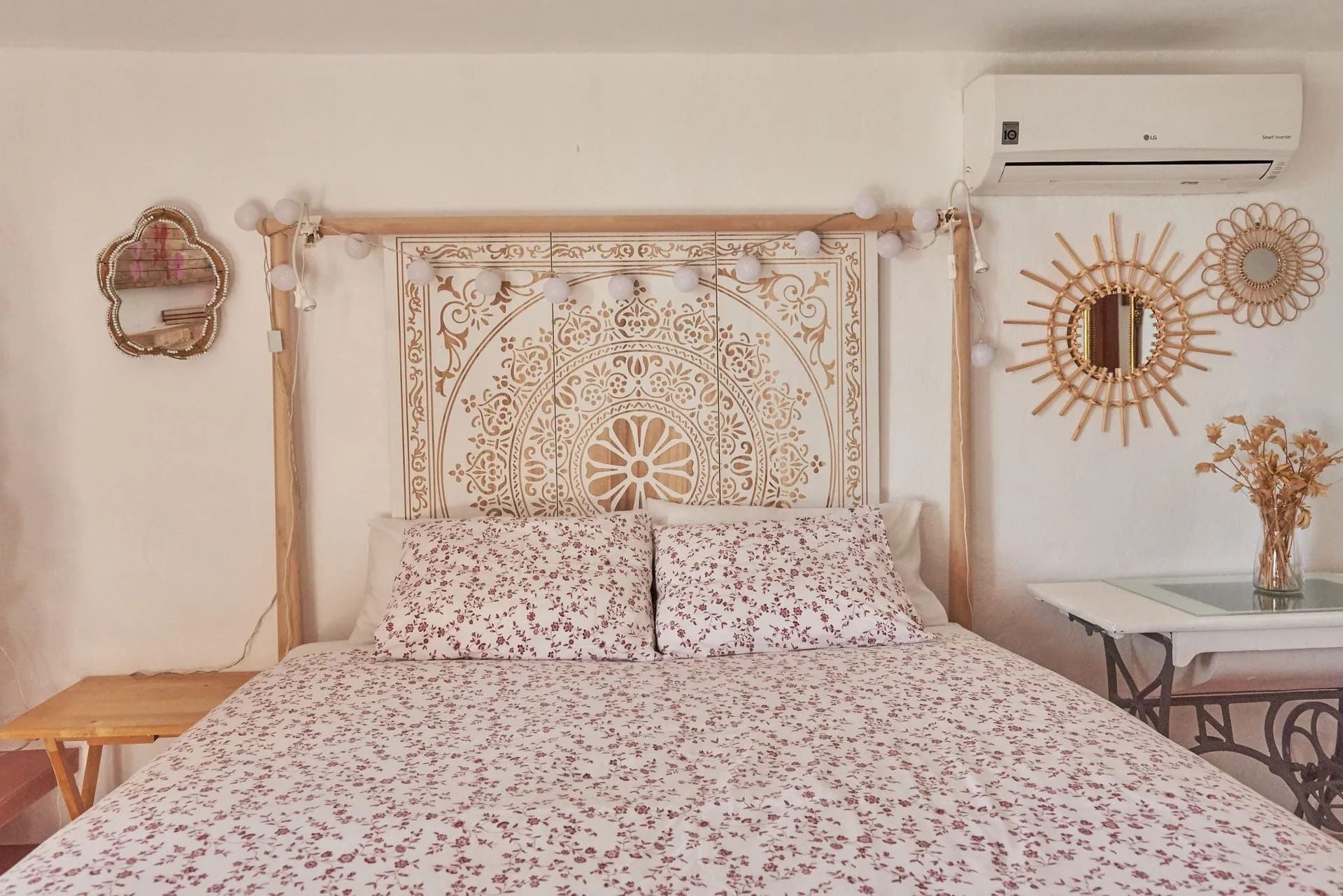 Dormitorio con cabecero de madera tallada, ropa de cama floral y espejos de pared decorativos.