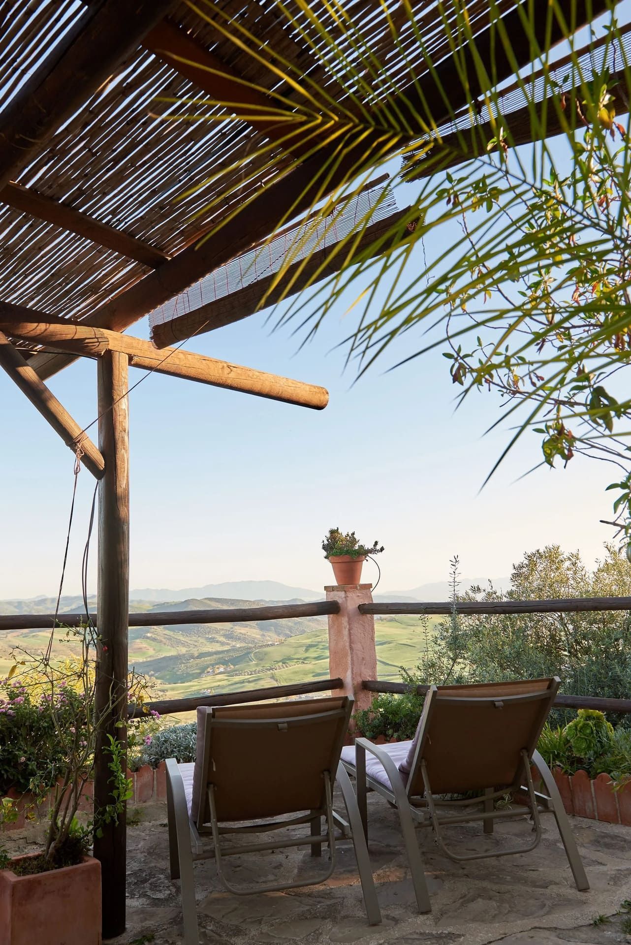 Dos tumbonas bajo una pérgola de madera con vistas a un pintoresco valle verde.
