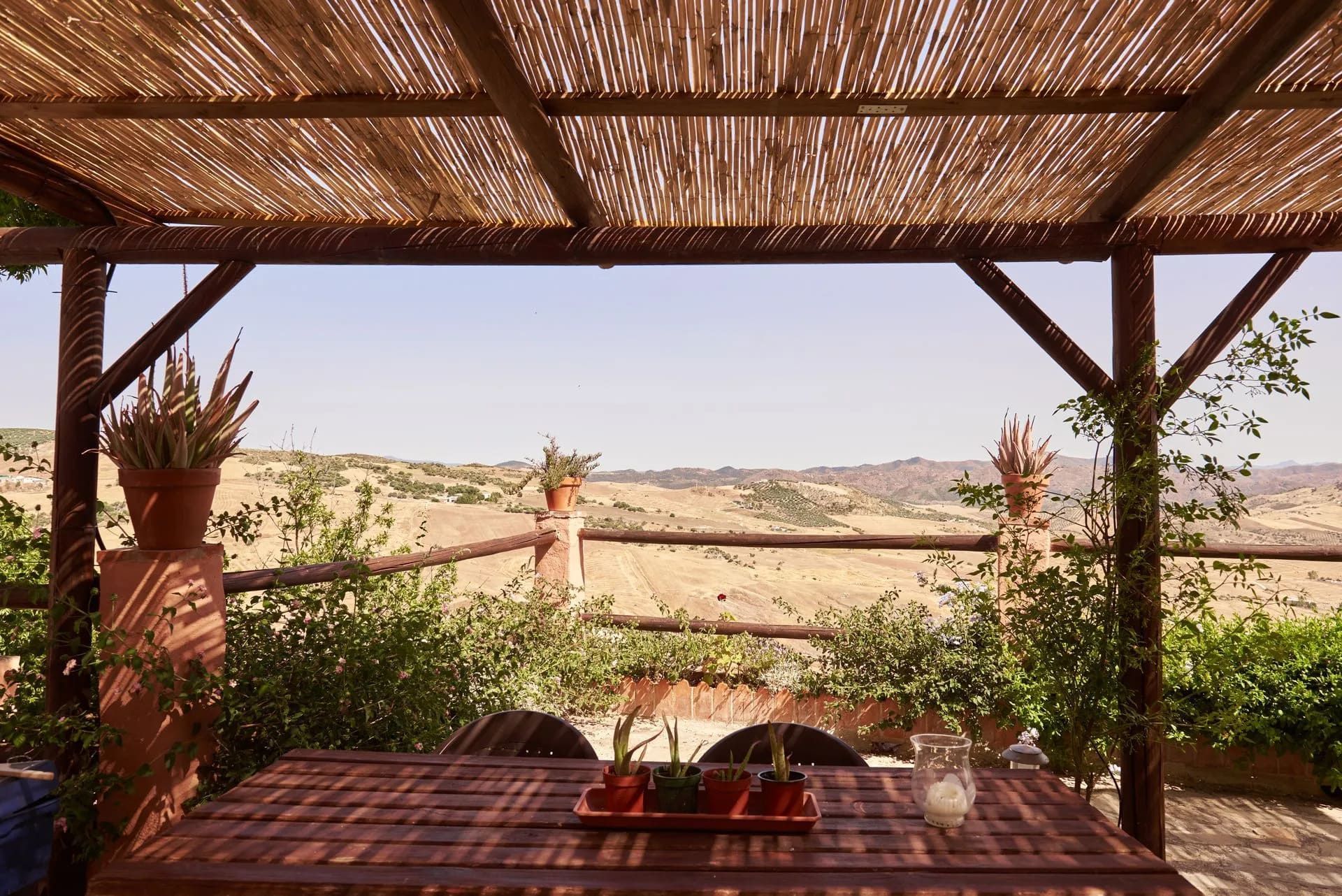 Pérgola de madera con mesa, con vistas a un paisaje rural.