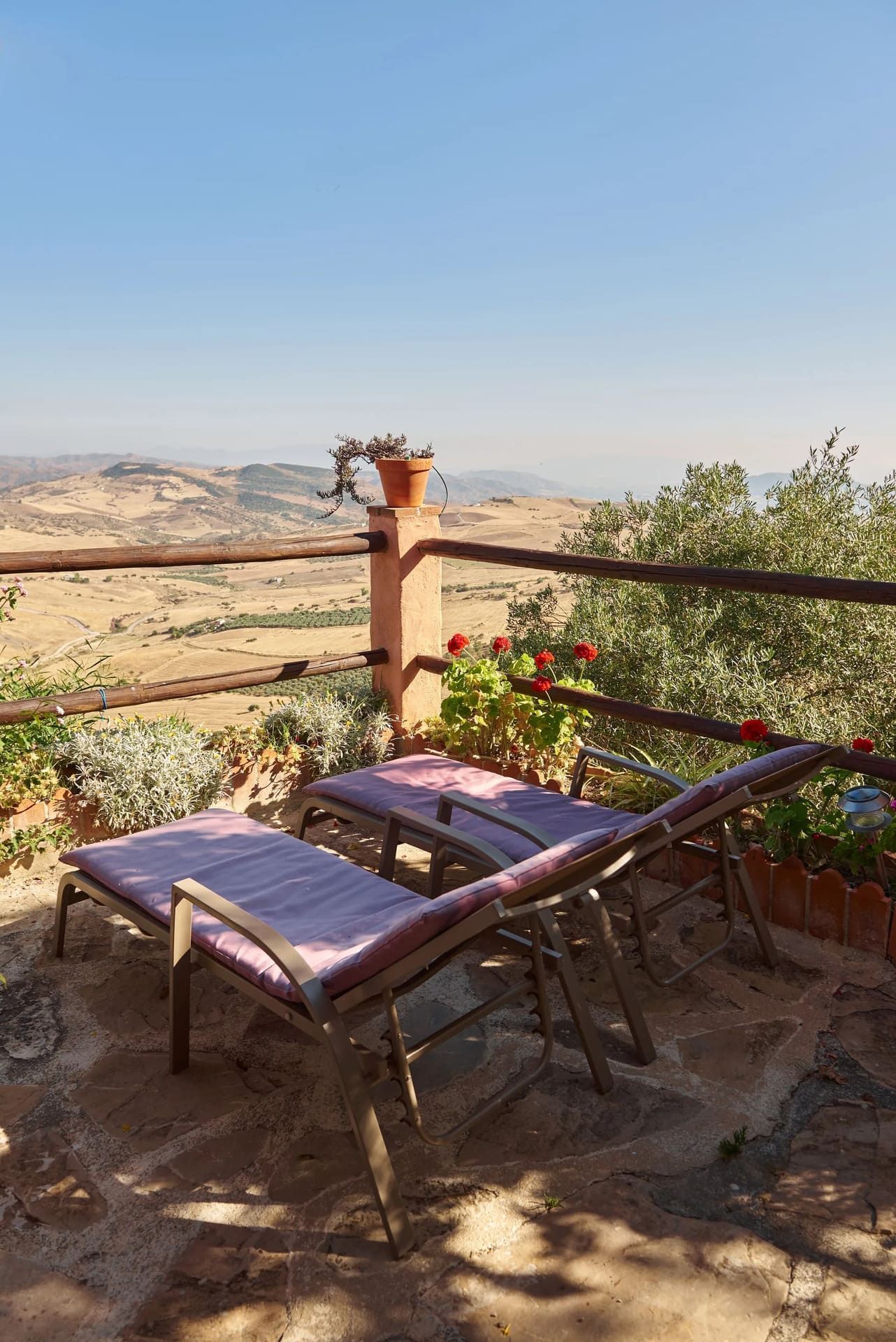 Dos tumbonas en un patio de piedra con vistas a un vasto y árido paisaje bajo un cielo despejado.