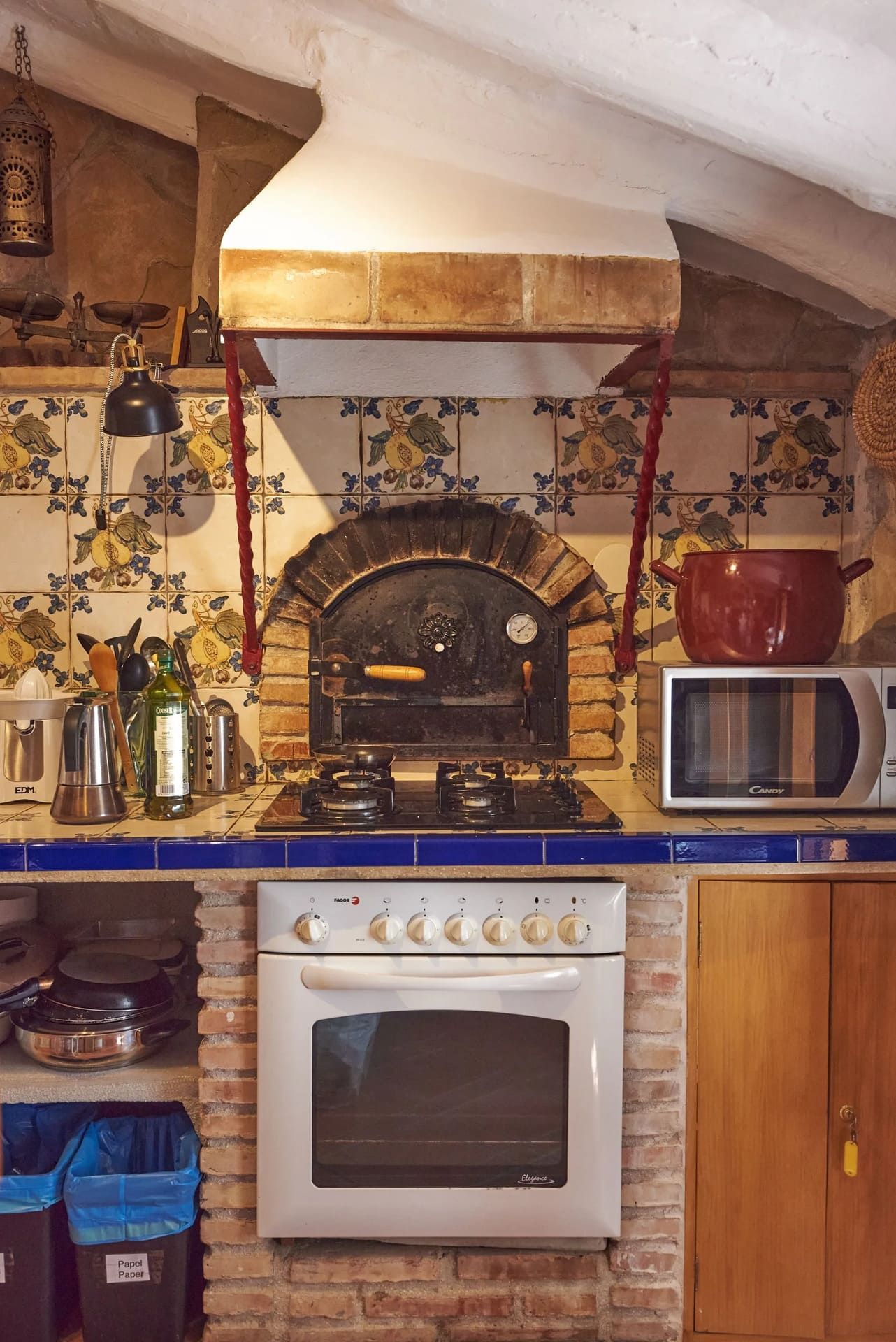 Cocina con horno, estufa, microondas y horno de pizza; ladrillo, azulejos y gabinetes de madera.