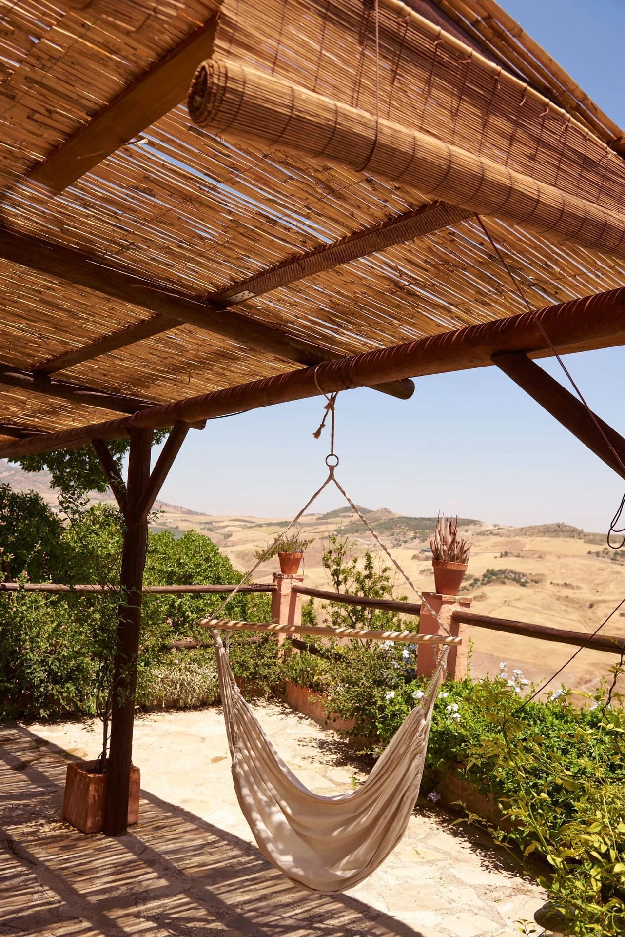 Hamaca bajo una pérgola de madera tejida con vista a un paisaje seco y montañoso.
