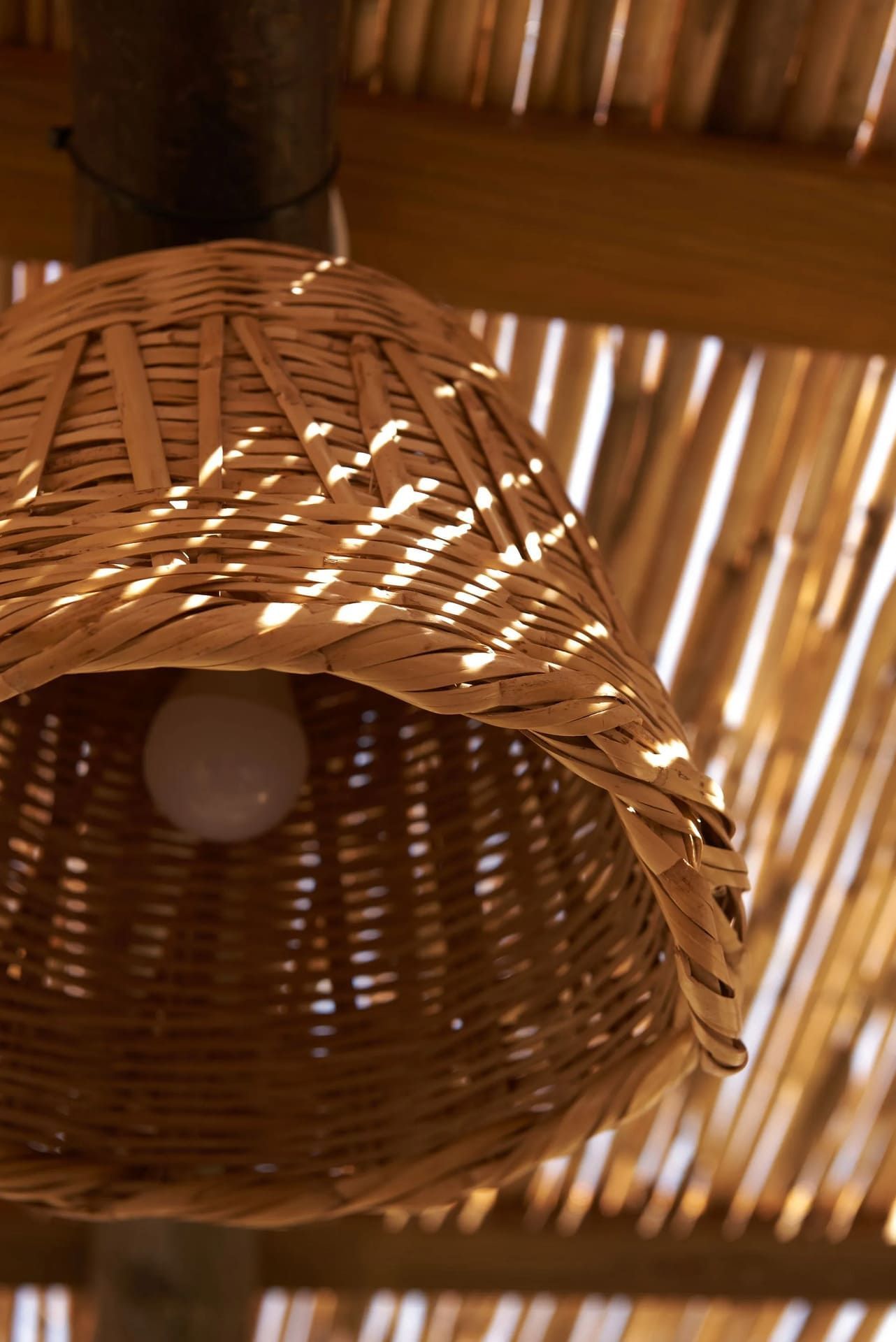 Pantalla de lámpara de mimbre tejido con una bombilla colgando de un techo de bambú.