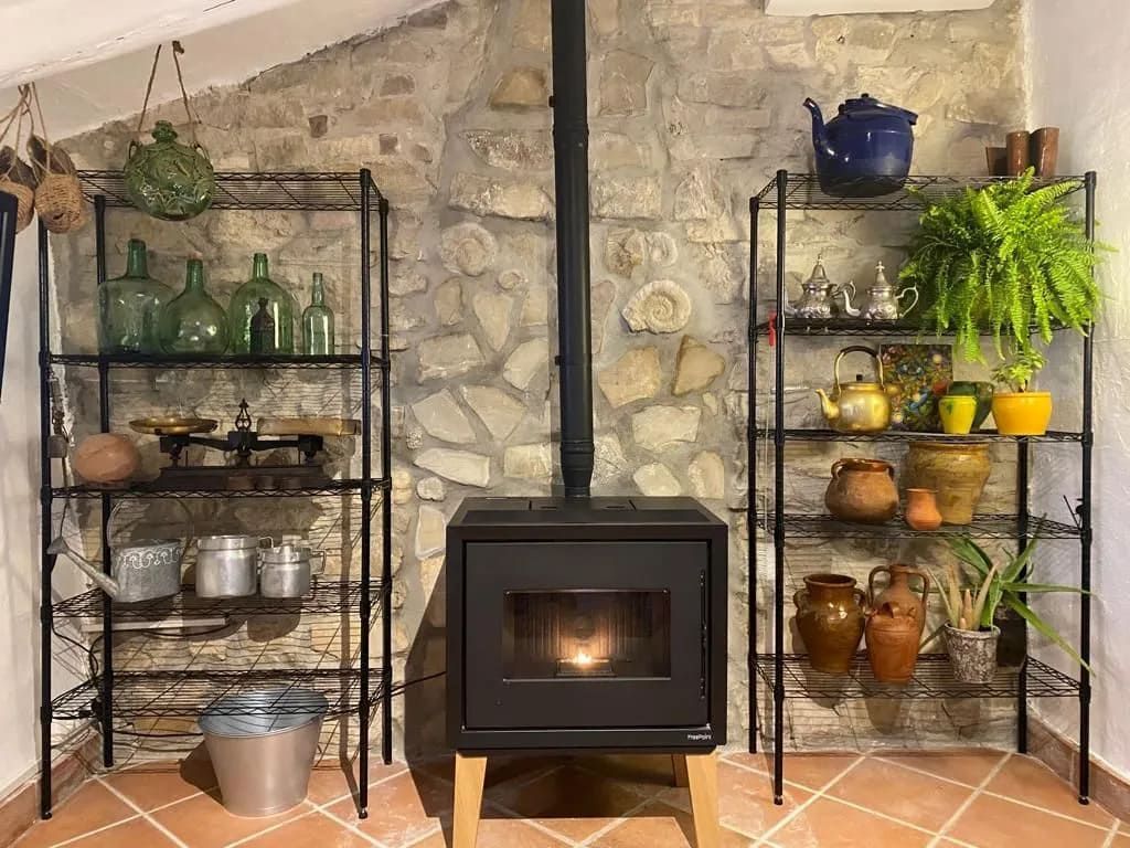 Chimenea con estantes contra una pared de piedra, que contiene plantas, teteras y artículos vintage.