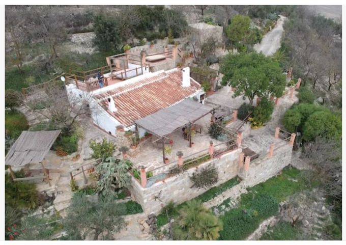 Casa rústica en ladera con tejado de tejas rojas, patio y jardín circundante.