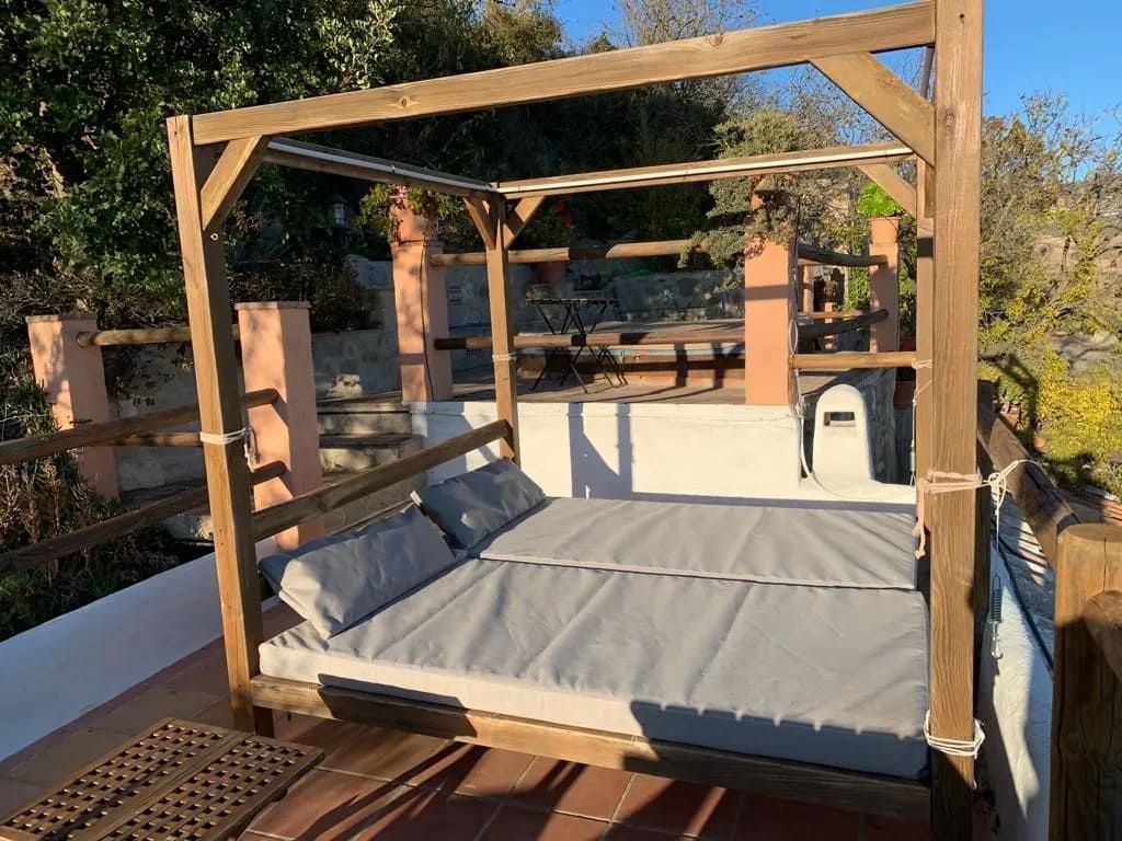 Diván de madera con cojines grises en patio con estructura de madera y estuco.