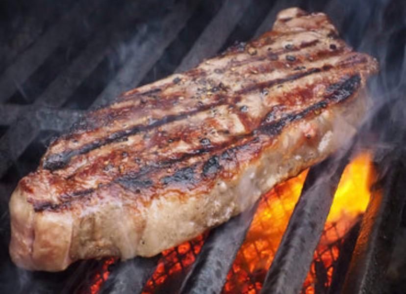 Un filete grueso con marcas oscuras de la parrilla, cocinado a fuego abierto en una parrilla de metal.