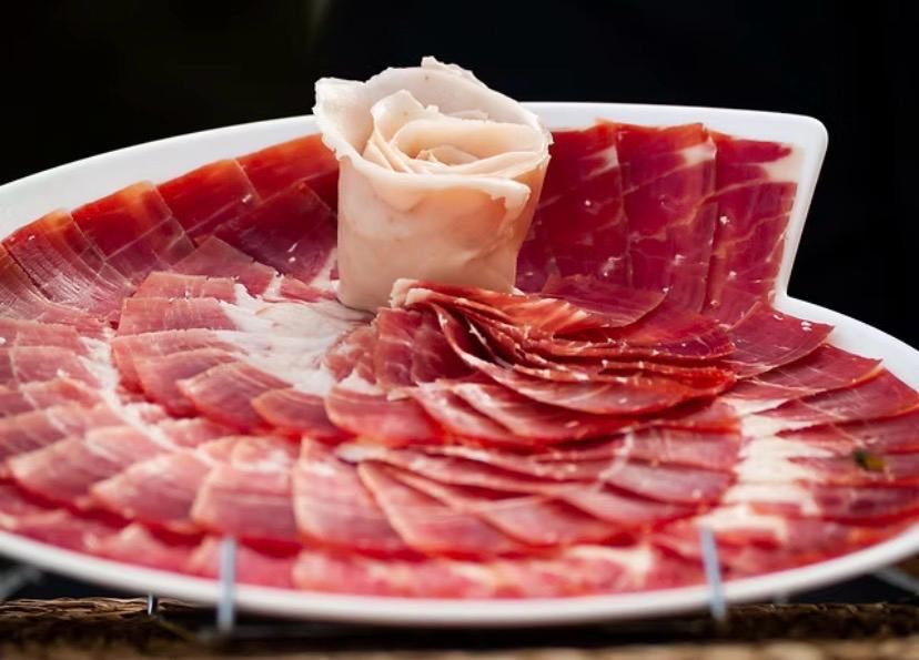 Jamón curado de color rojo intenso, cortado en lonchas finas y dispuesto en forma de abanico circular 