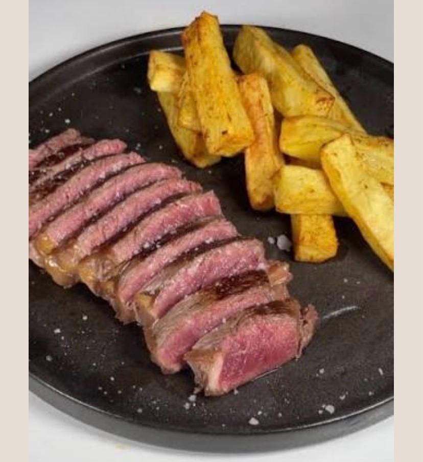 Un plato negro contiene filete poco hecho en rodajas, junto a una montaña de patatas fritas doradas