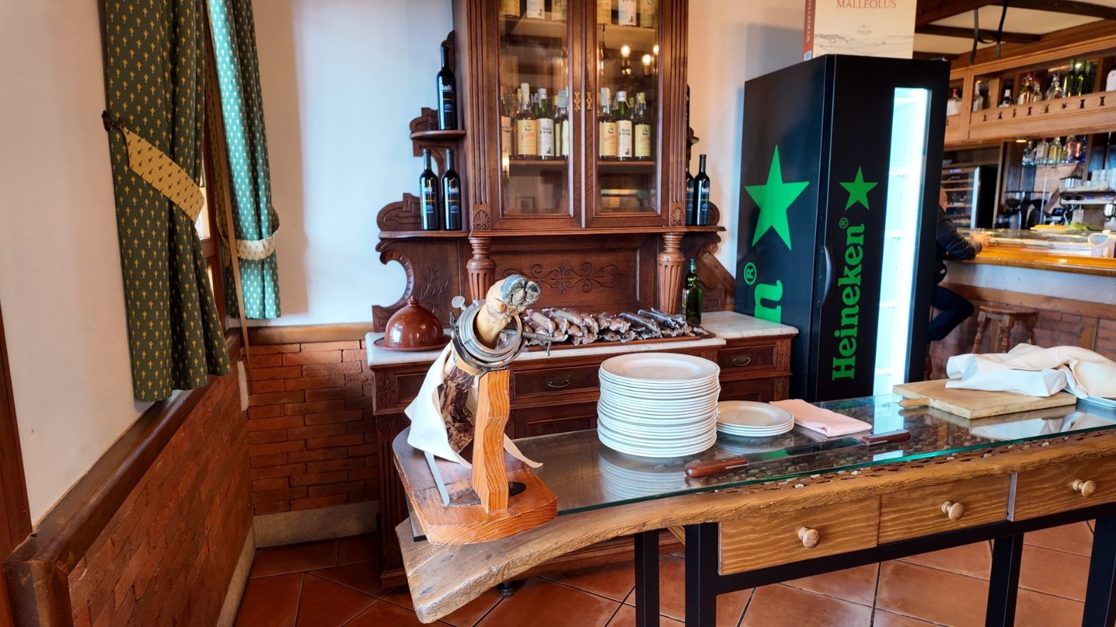 El interior de un restaurante con una pierna de jamón sobre un soporte de madera, una vitrina 