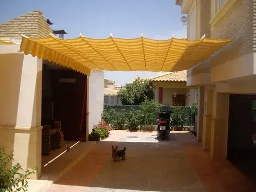 Un perro se sienta bajo un toldo amarillo en una entrada.