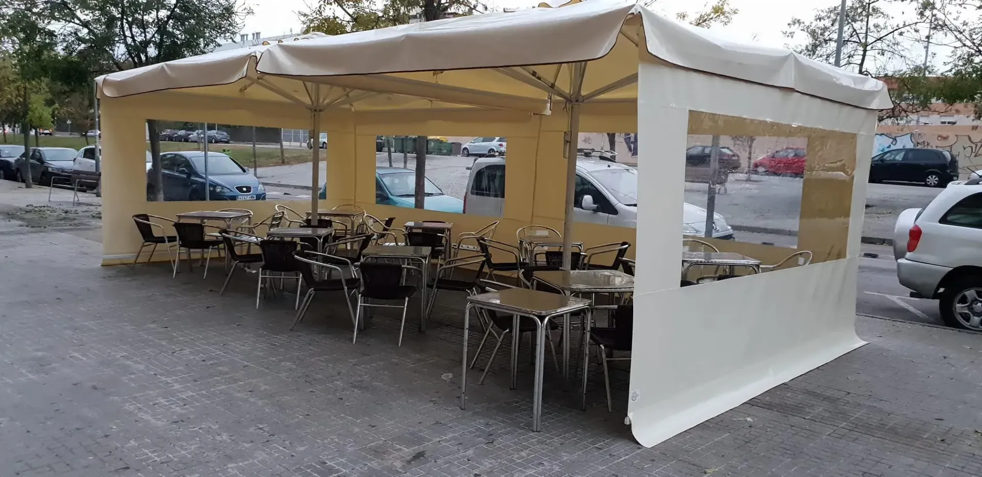 Una fila de mesas y sillas debajo de una carpa en un estacionamiento.