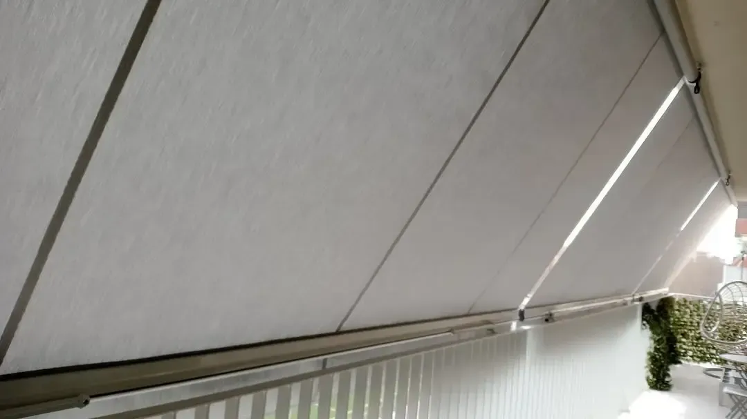 Un toldo blanco cubre un balcón con barandilla de rayas.